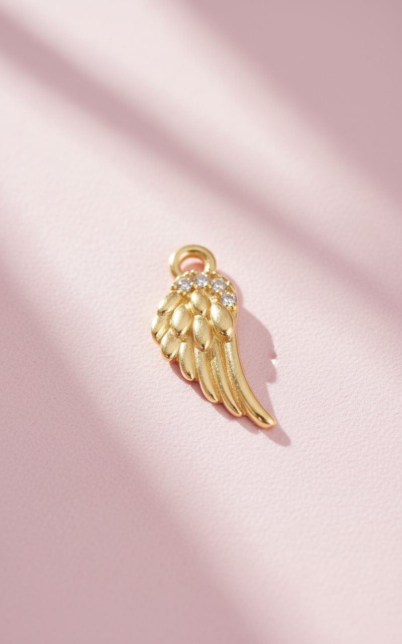 Gold angel wing charm with rhinestones on a pink background