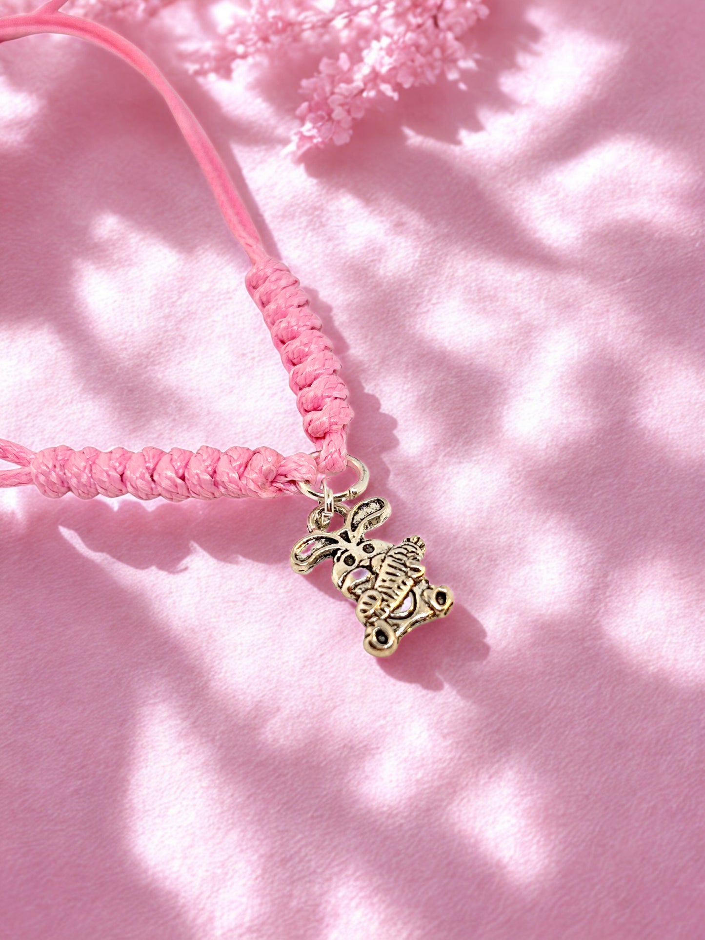 Pink cord bracelet with a silver bunny charm on a pink background