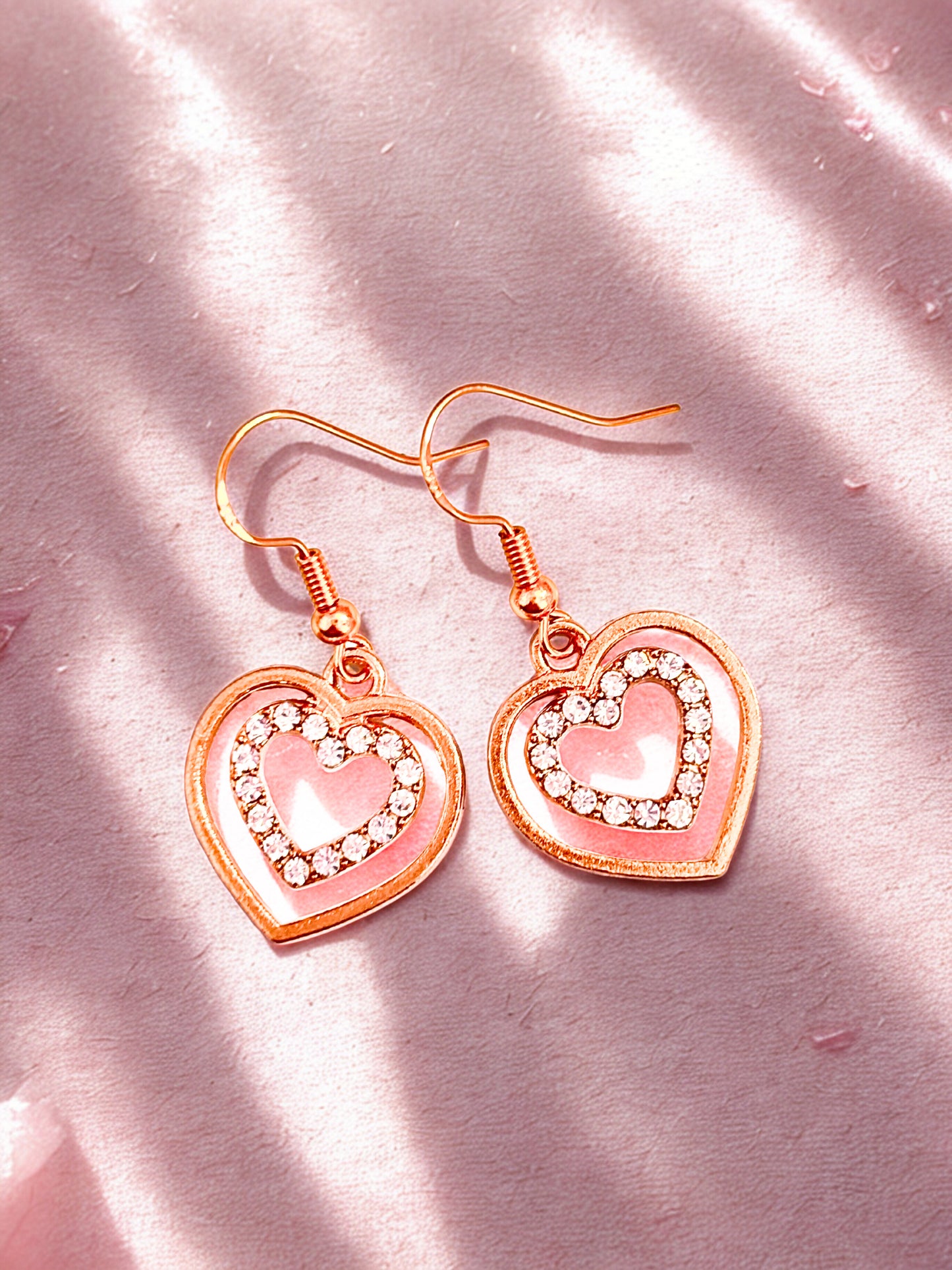 Heart-shaped earrings gold accents on a pink fabric background