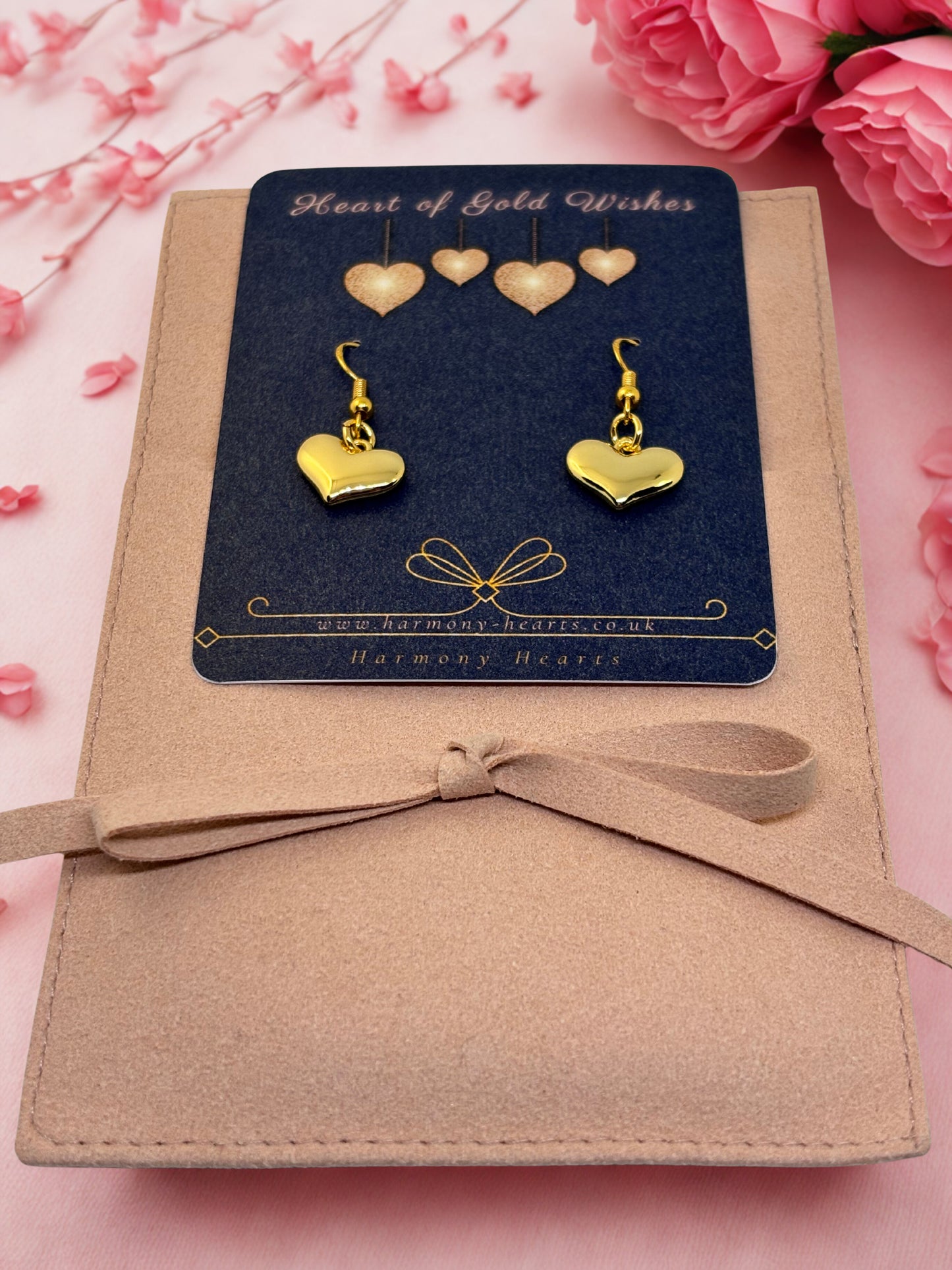 Heart-shaped gold earrings on a 'Heart of Gold Wishes' card with pink flowers in the background.