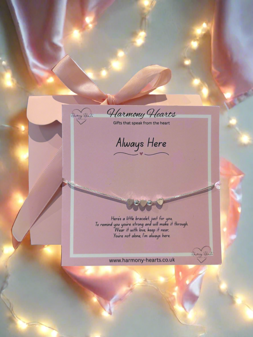 Silver bracelet with heart charms on a pink card with 'Harmony Hearts' branding, surrounded by fairy lights.