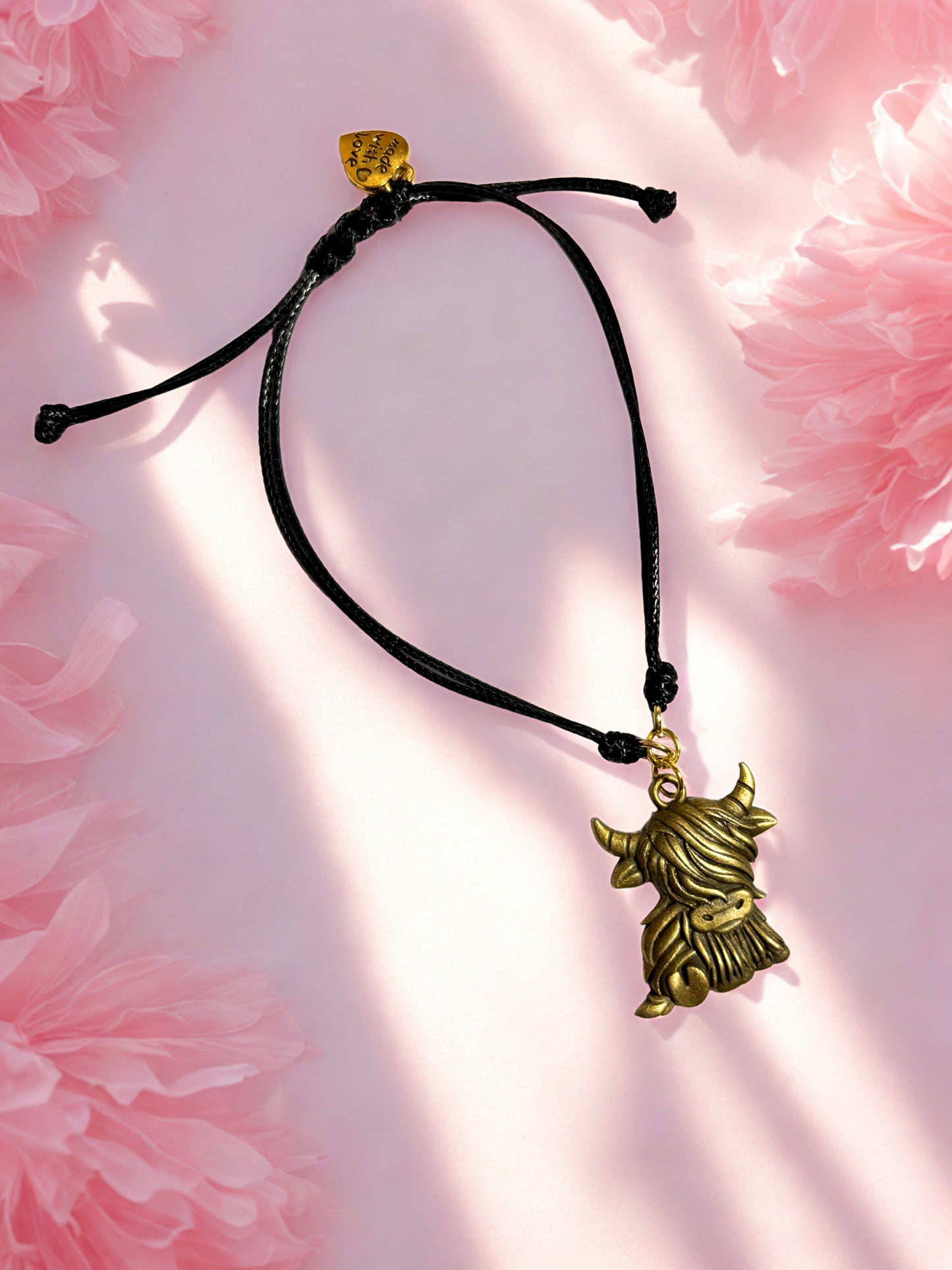 Bracelet with a bronze highland cow charm on a pink floral background