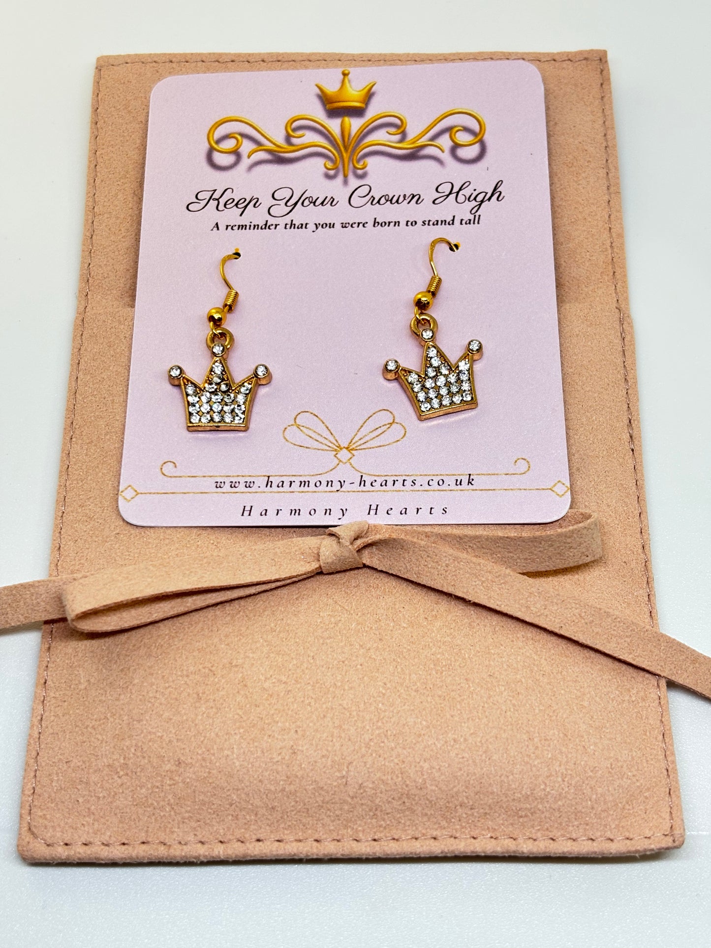 Crown-shaped earrings on a 'Harmony Hearts' card with a beige bow