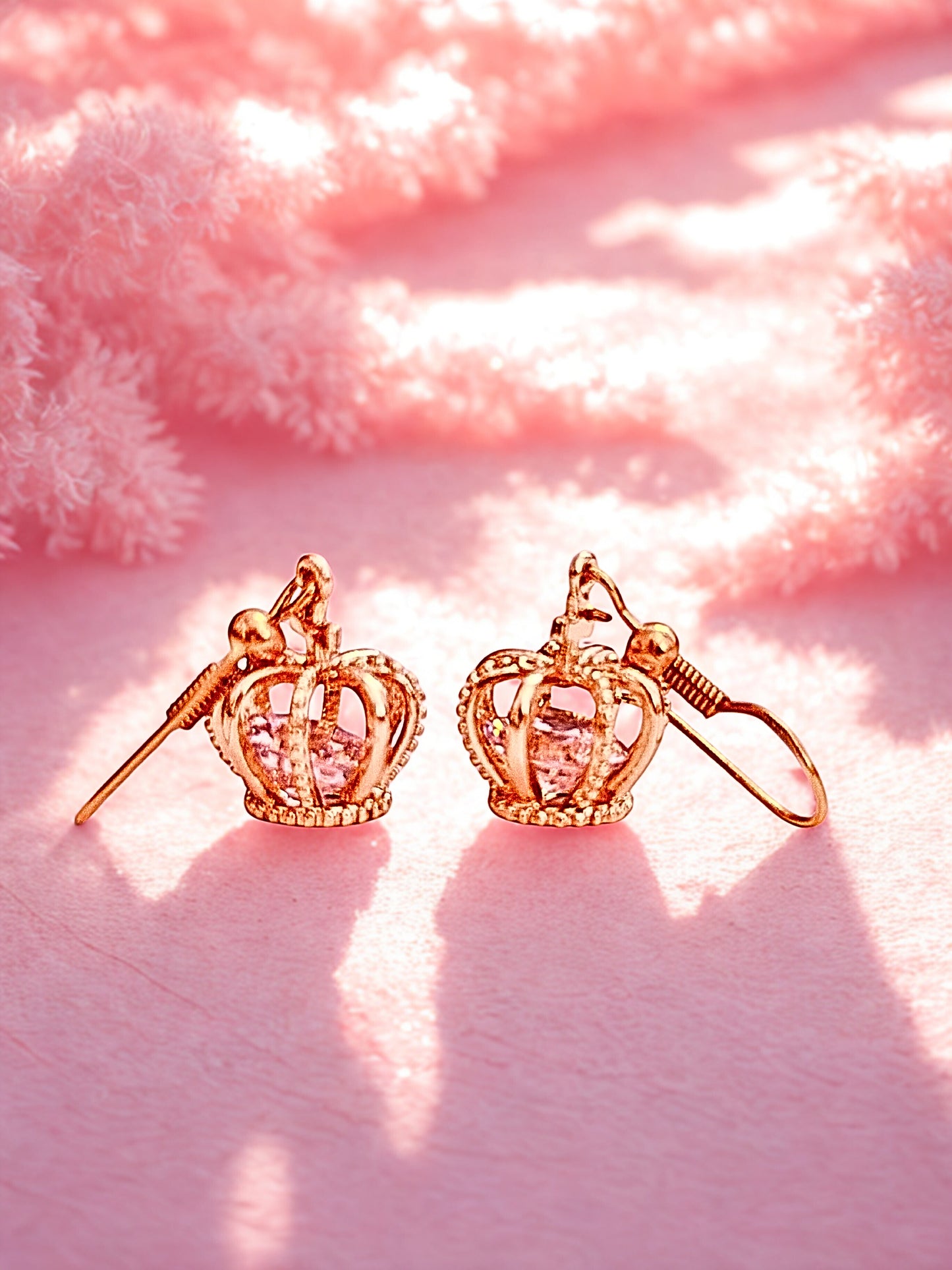 gold crown drop earrings on a pink surface