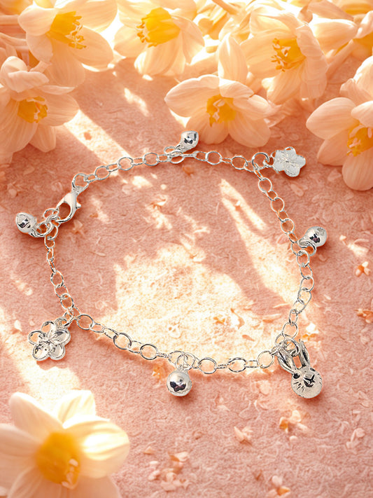 Silver charm bracelet with bunny and flower charms laid on a pink surface