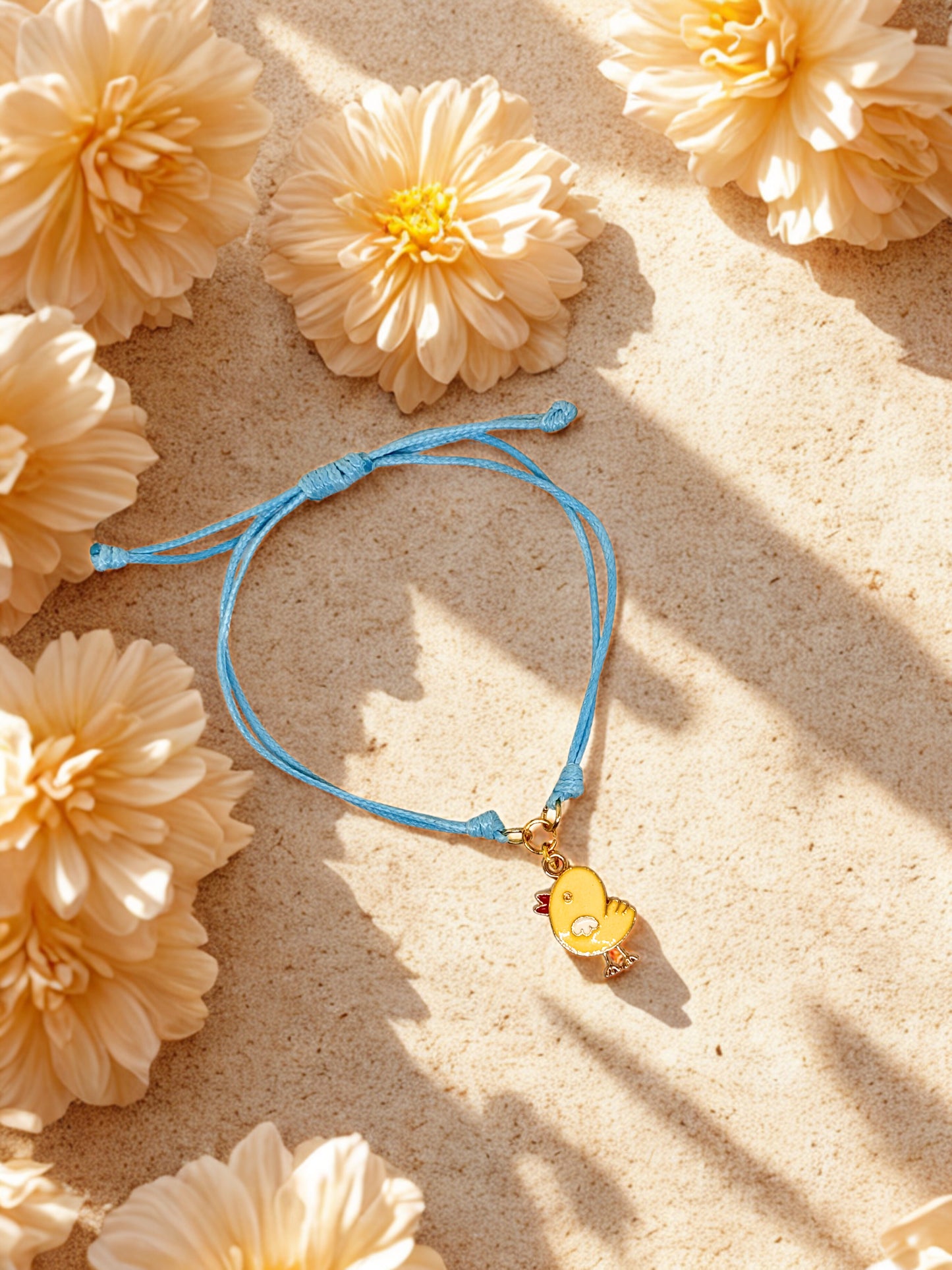 Blue bracelet with a yellow chick charm on a sandy background with yellow flowers