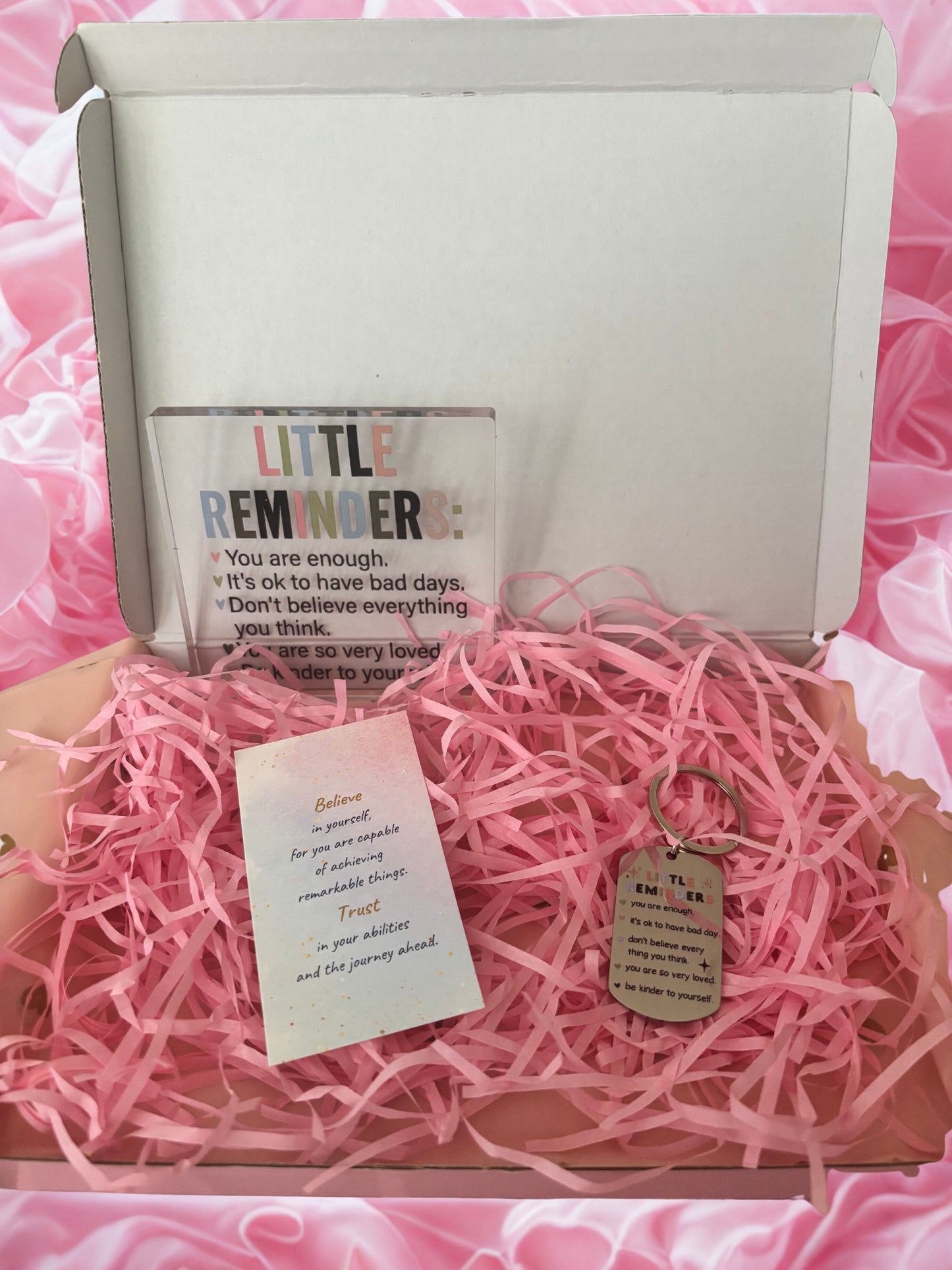 Gift box with pink interior, containing a bottle labeled 'Little Reminder' and a keychain with a tag.