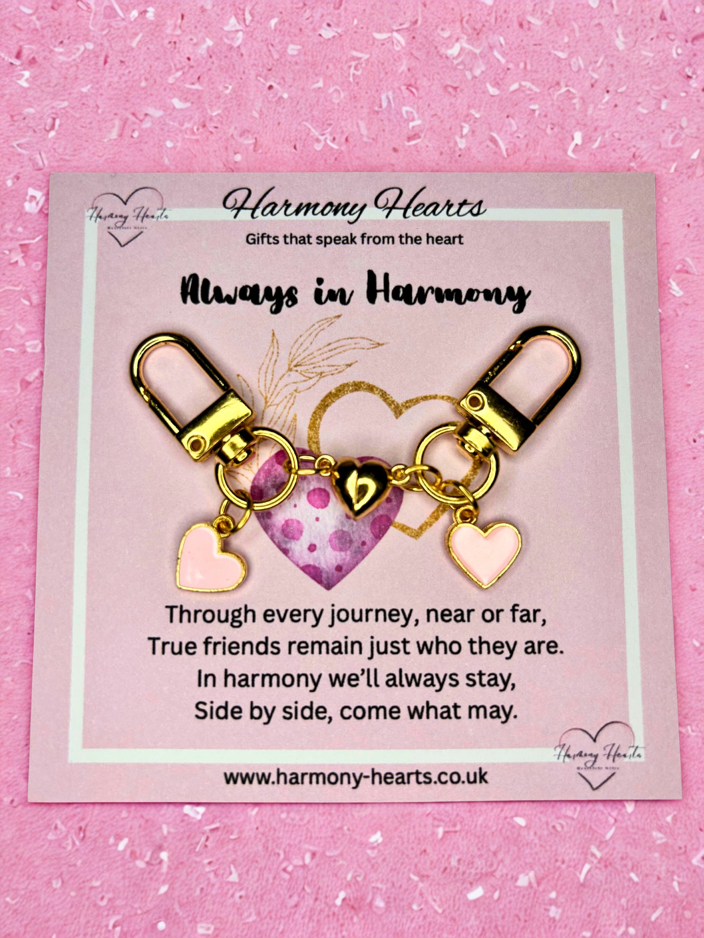 Gold heart-shaped keychain with charms on a pink card with text, against a pink background.