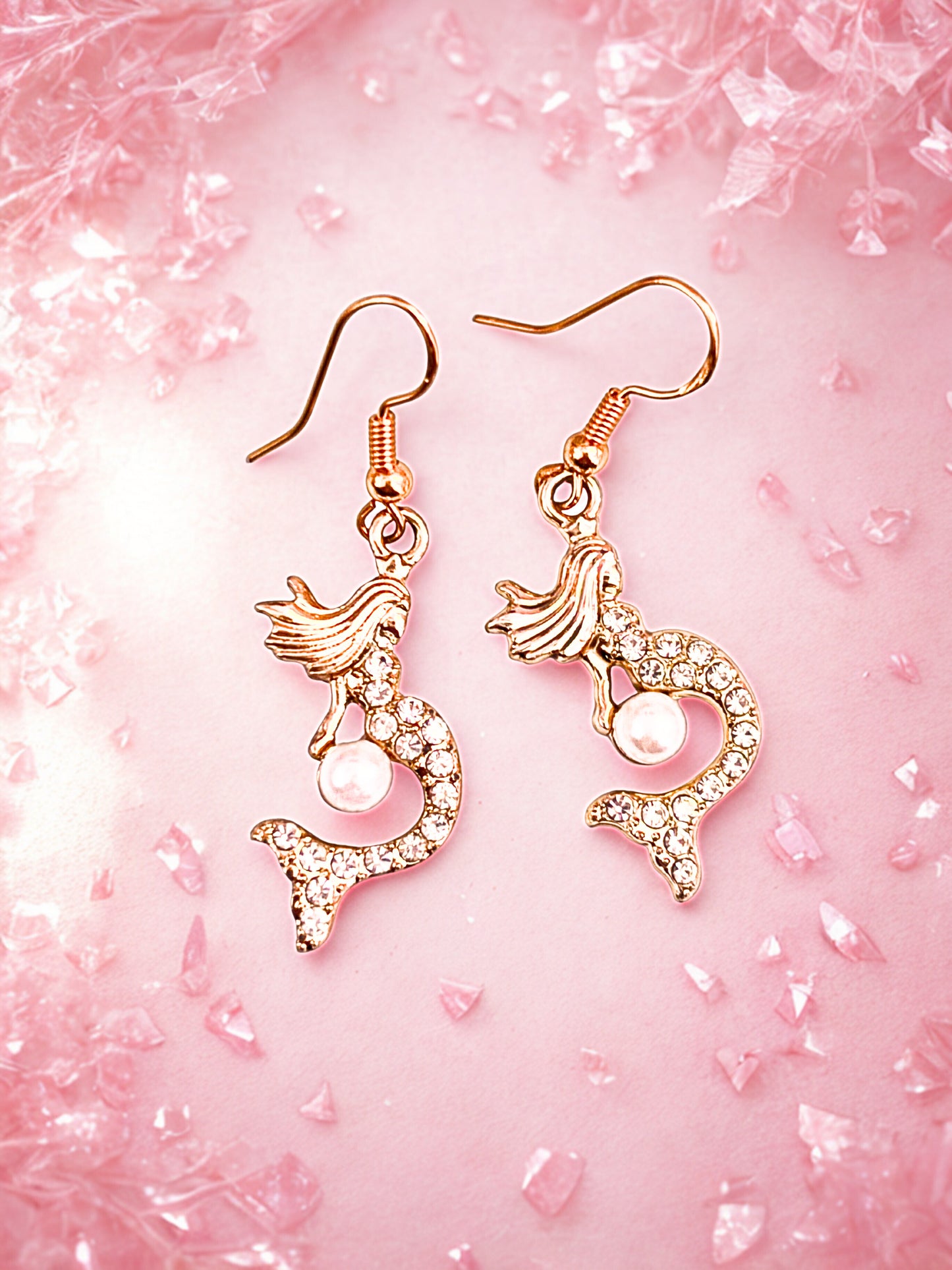 Mermaid-shaped earrings on a pink textured background