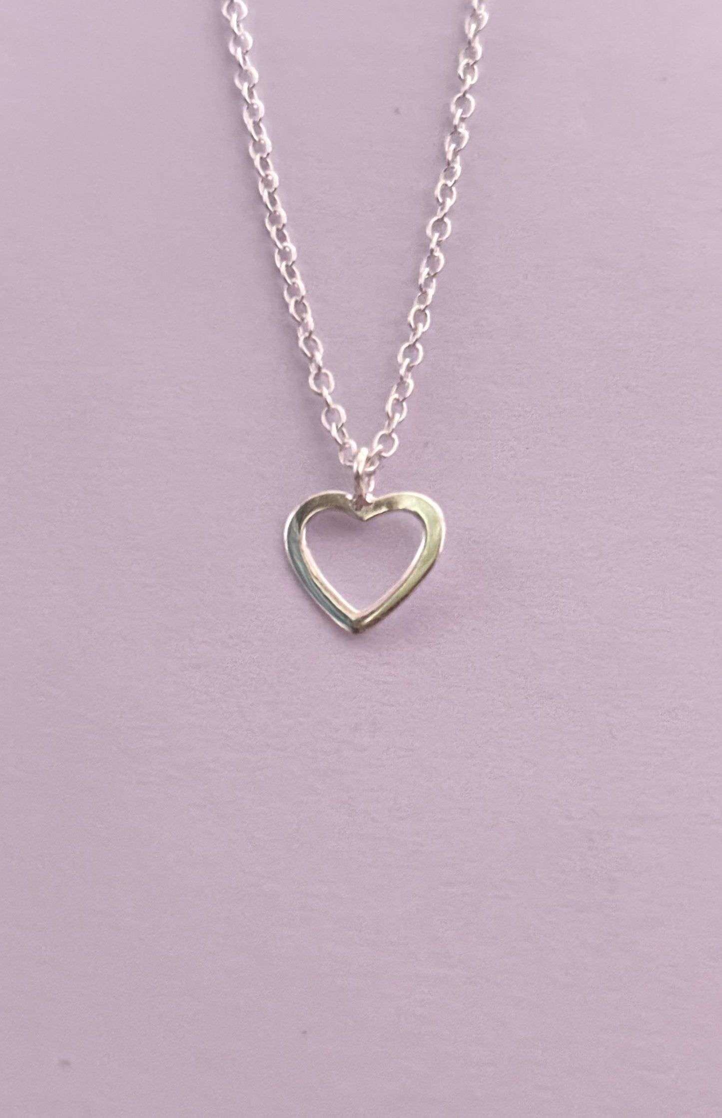 Silver heart-shaped pendant necklace on a light purple background