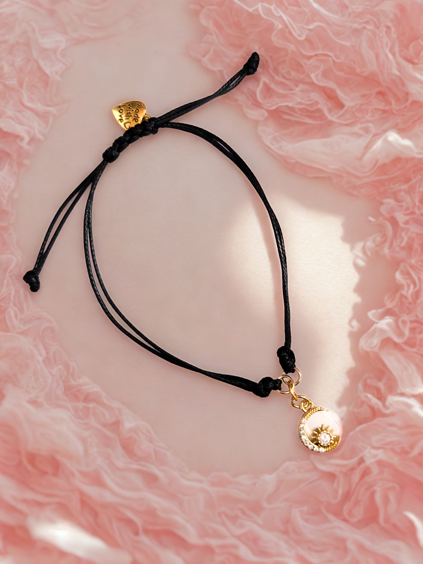 Black cord bracelet with gold moon charms on a pink marble background
