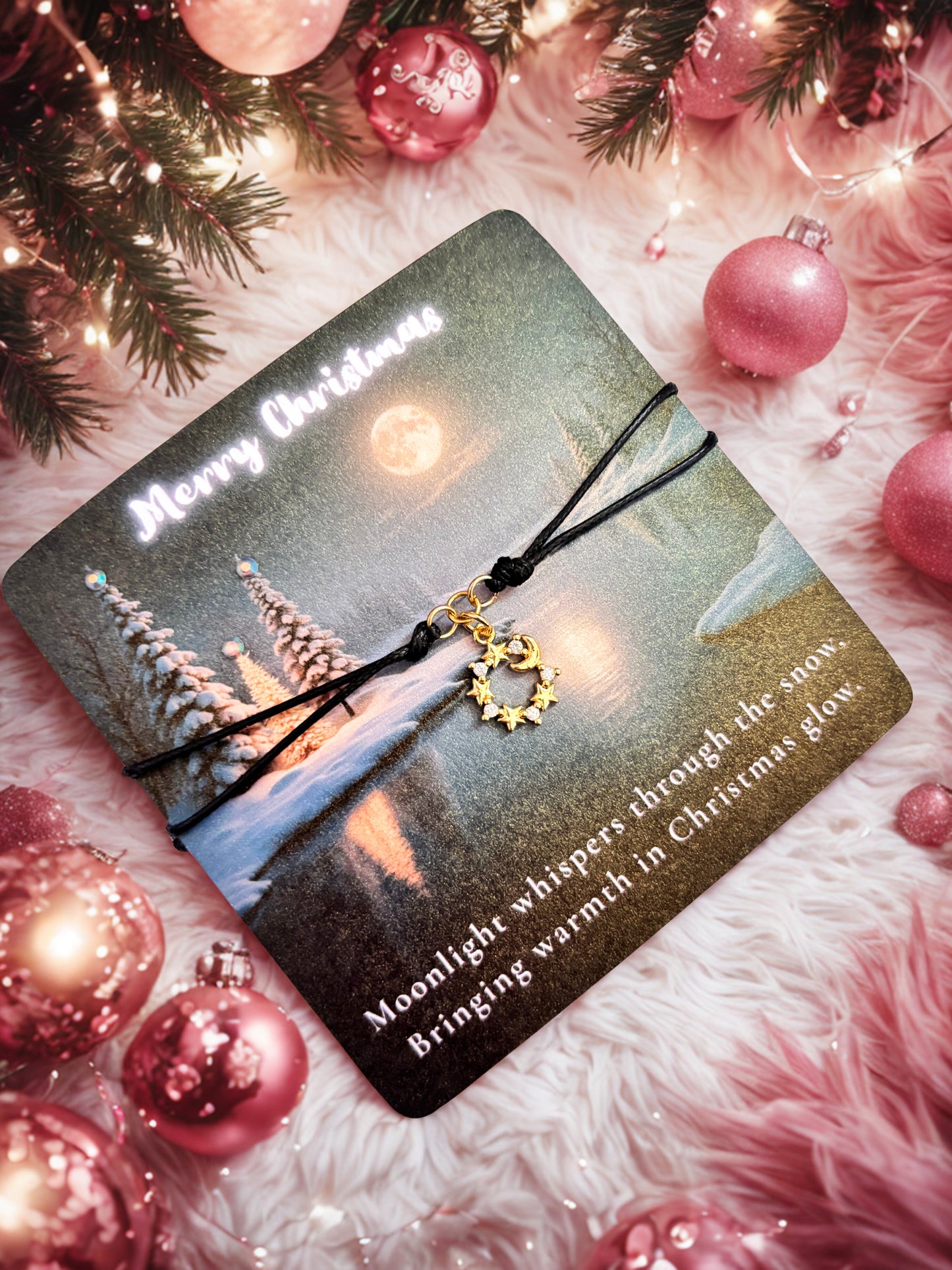 Bracelet with a moon and star charm on a Christmas-themed card surrounded by pink ornaments and lights.