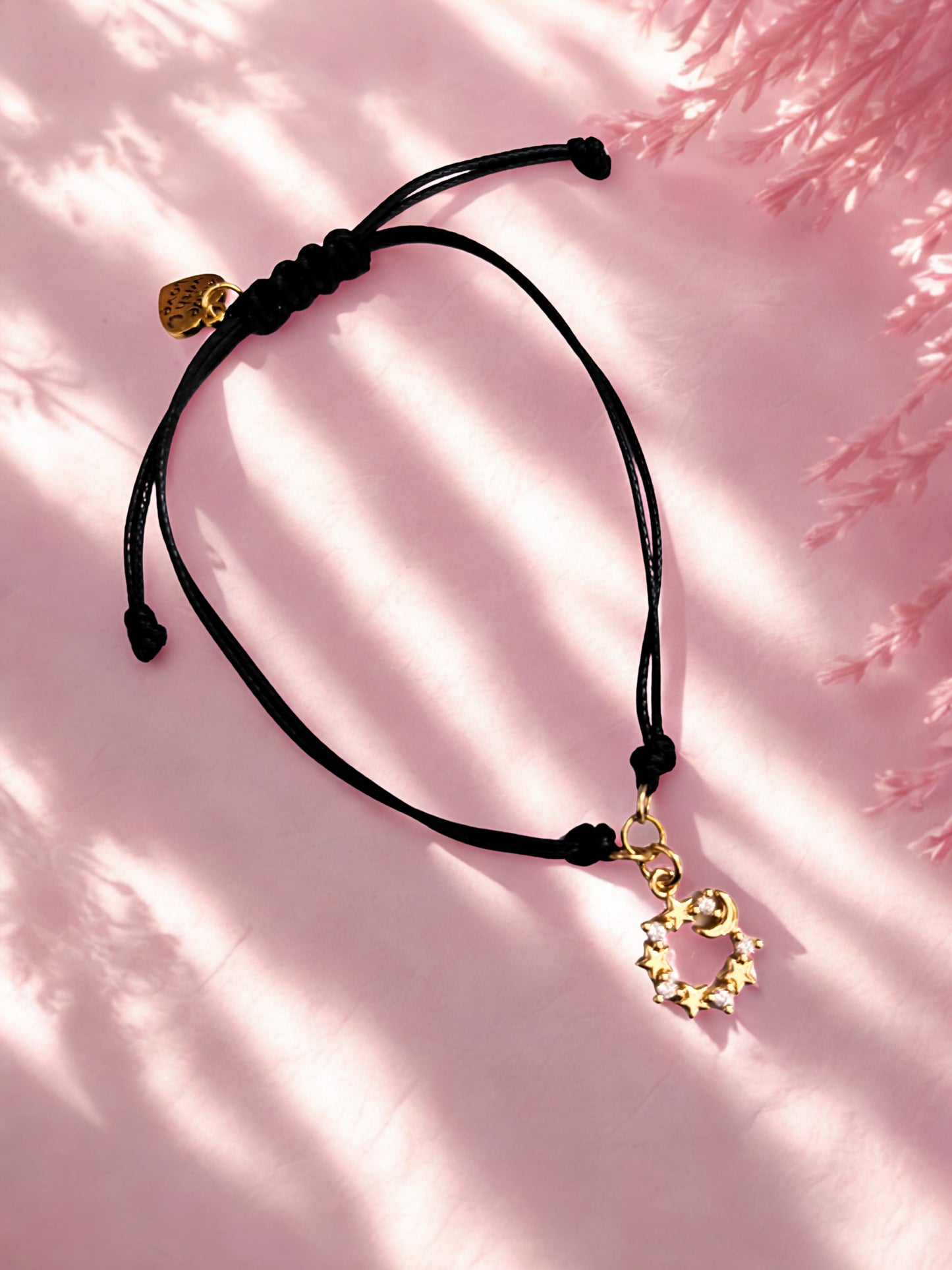 Black cord bracelet with gold moon and stars charm on a pink background