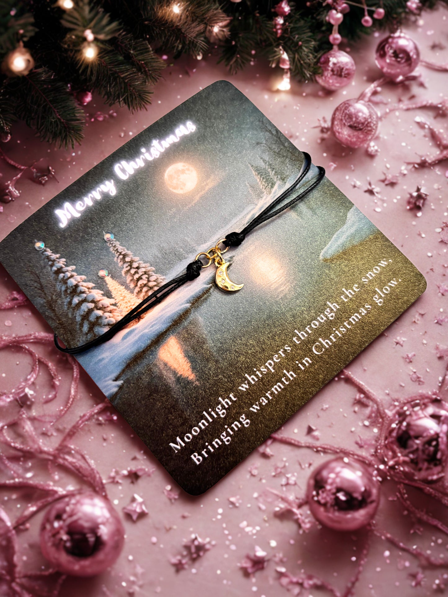 Gold moon charm on a decorative card with a Christmas theme on a pink background with ornaments