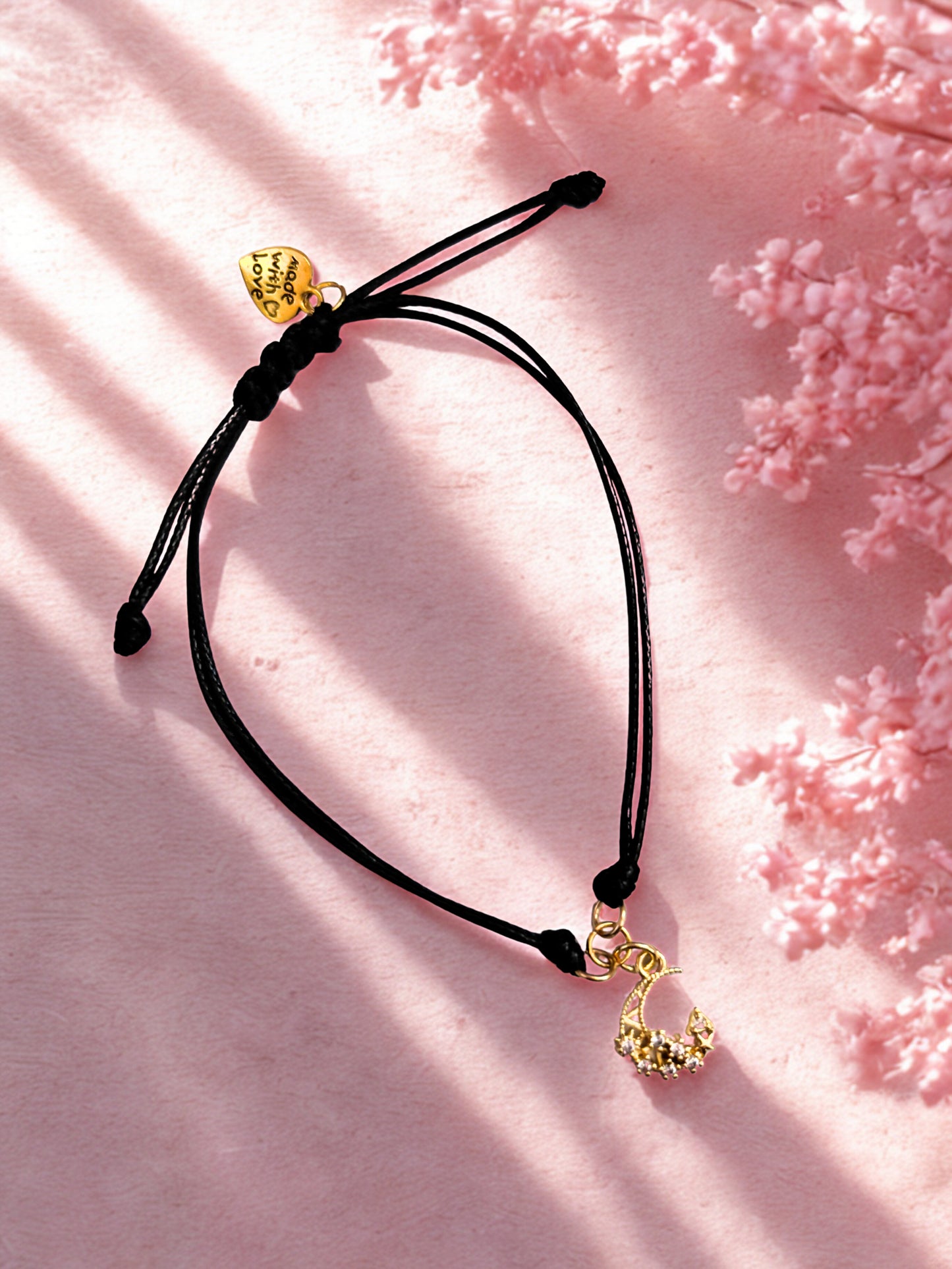Black cord bracelet with gold moon charm on a pink floral background