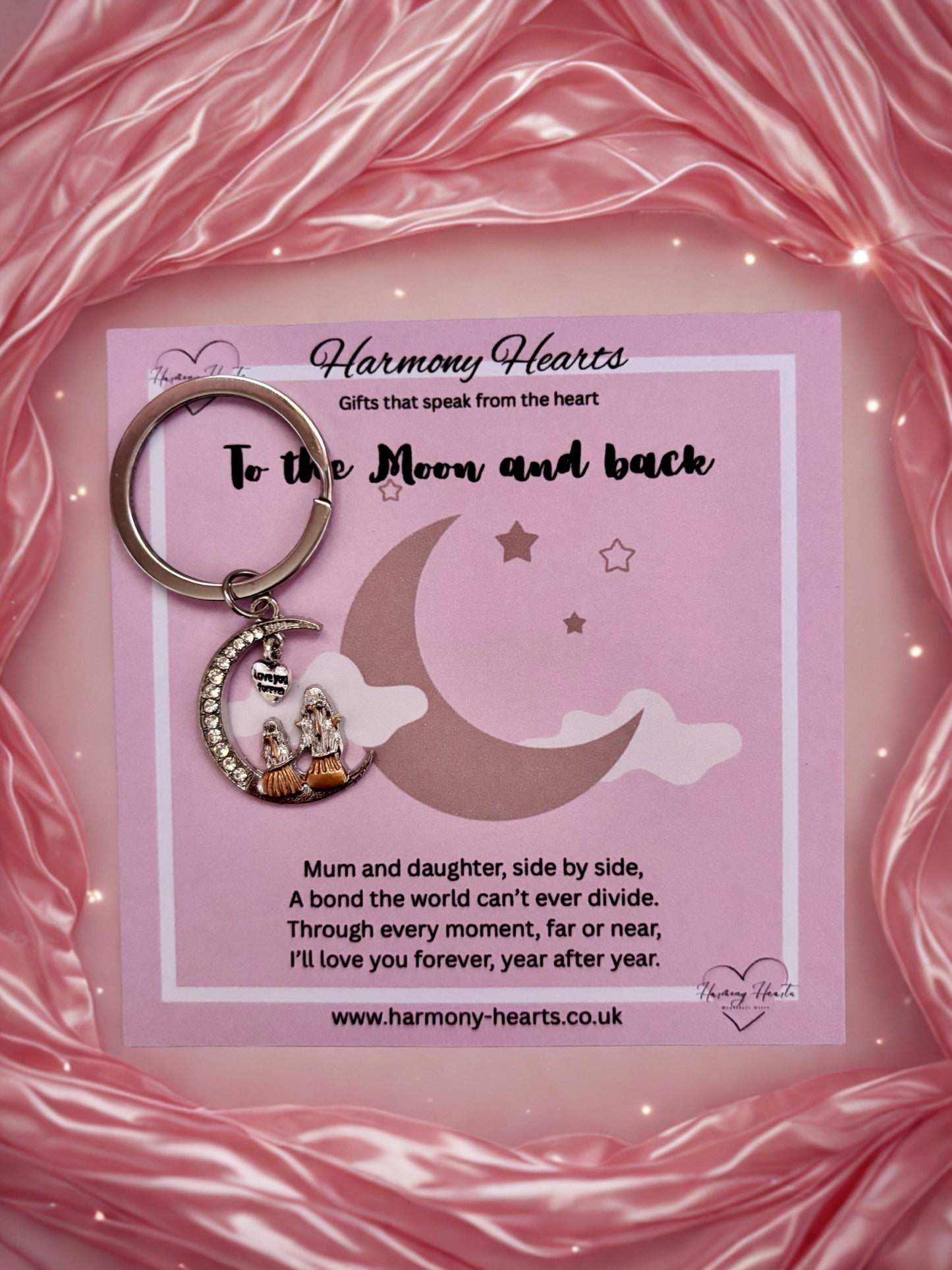 Keychain with moon and star design on a pink card with text, against a pink fabric background.