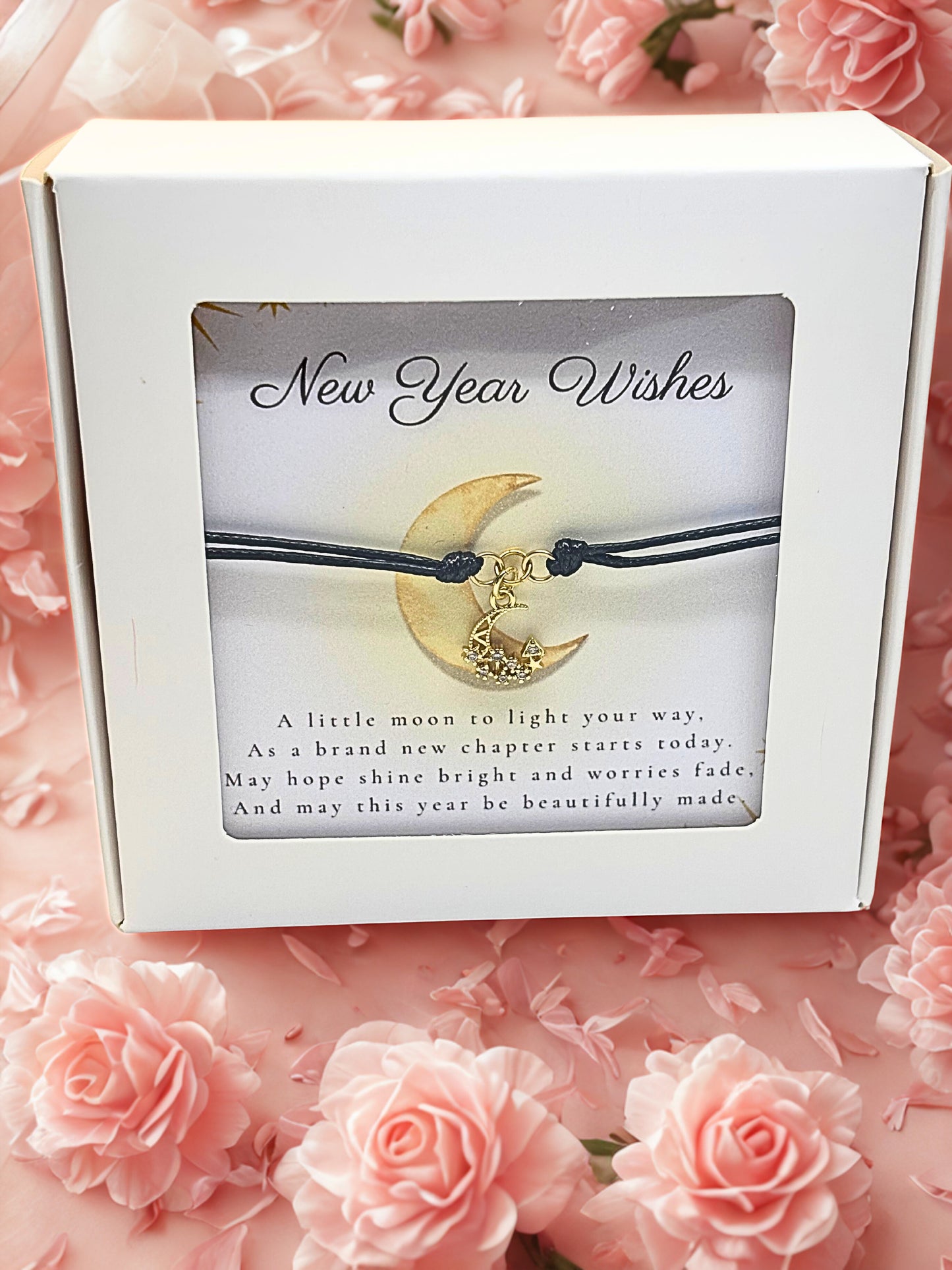 Box with 'New Year Wishes' card featuring a moon and star design braceelt on a pink floral background.