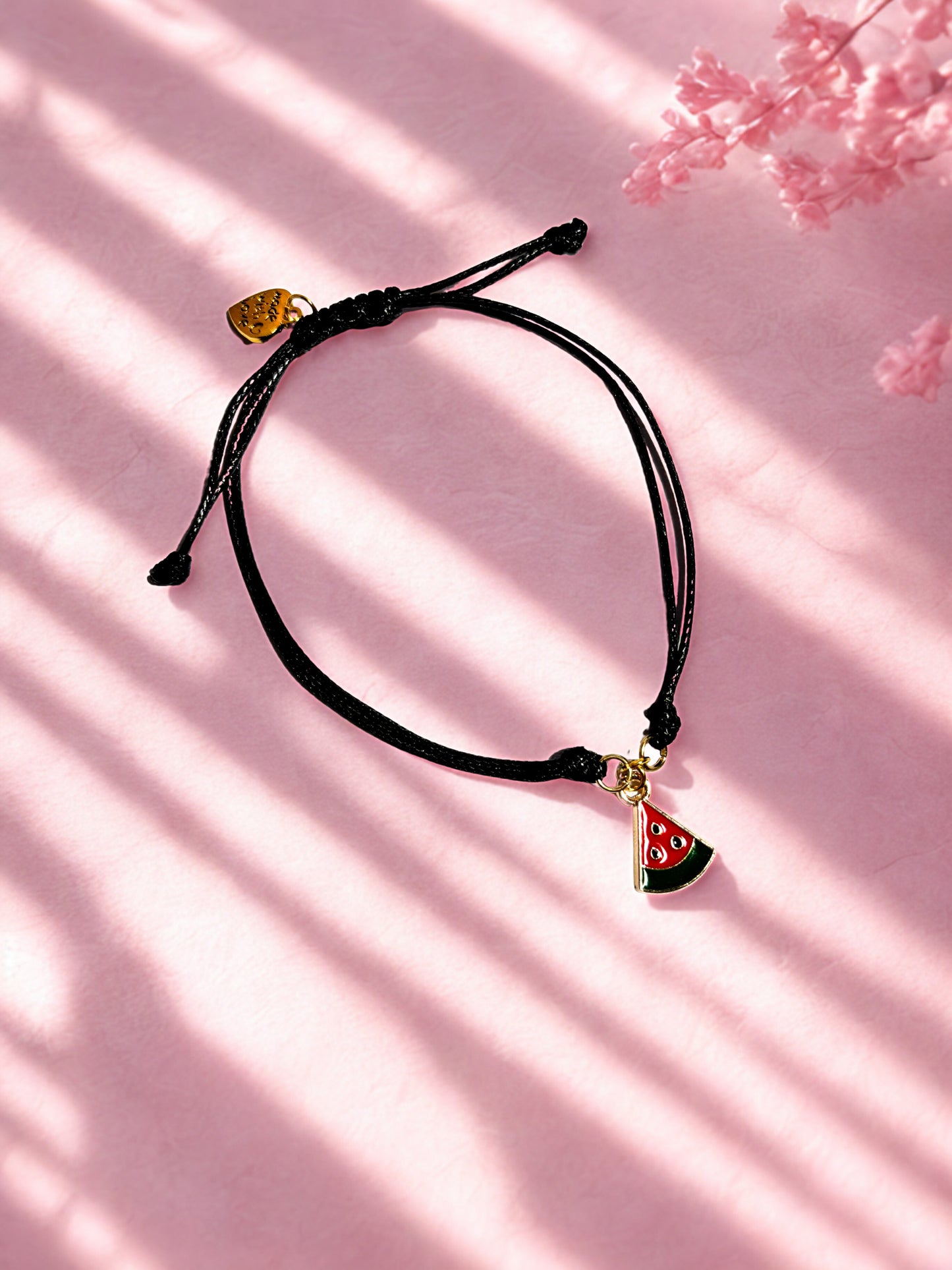 Black cord bracelet with a watermelon charm on a pink background