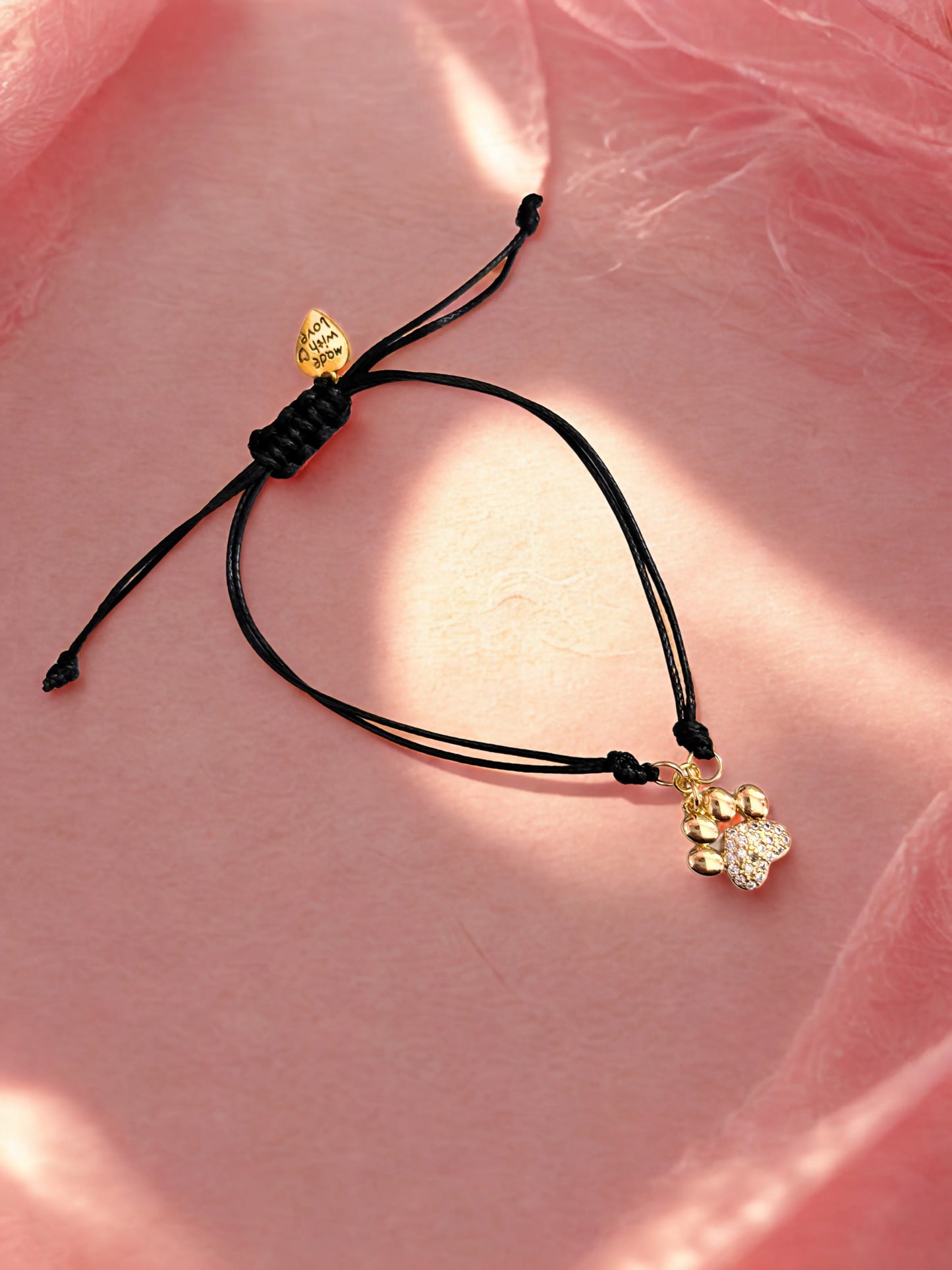 Black cord bracelet with gold and silver paw charm on a pink fabric background