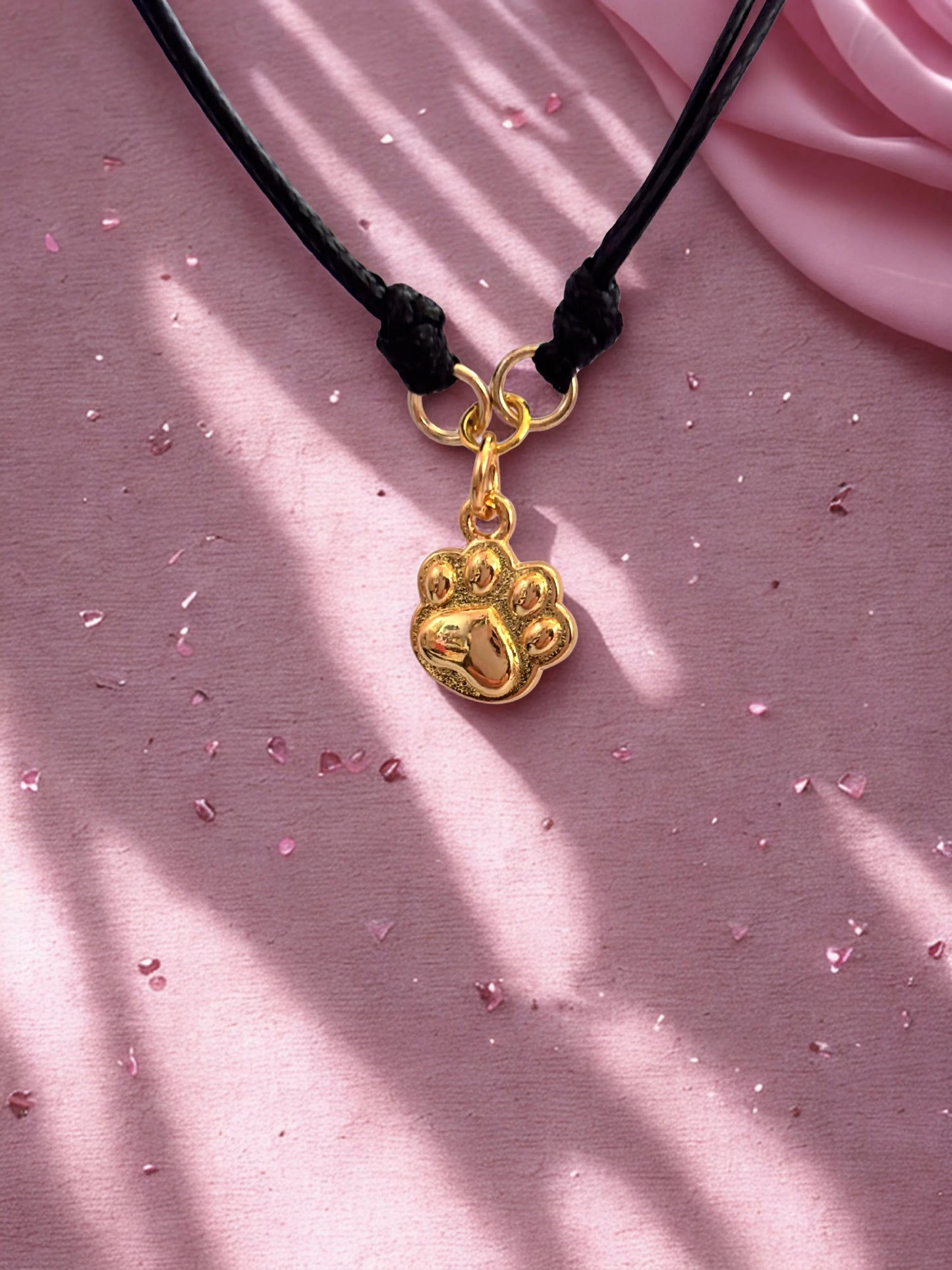 Gold paw-shaped charm on a black cord against a pink fabric background