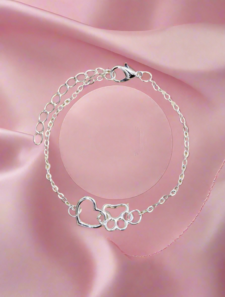Silver bracelet with heart and dog paw design on a pink fabric background