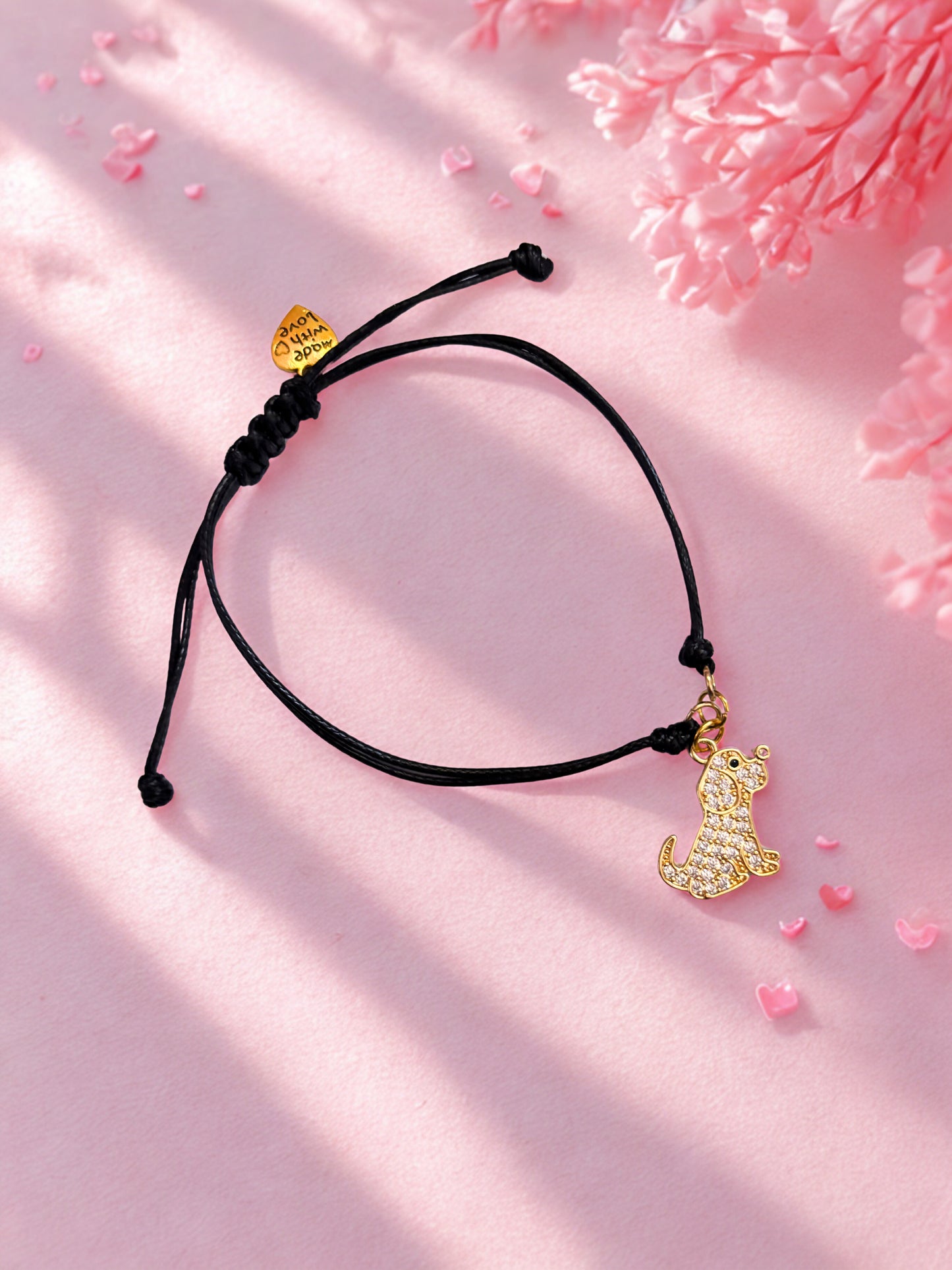 Black cord bracelet with gold dog charm on a pink background