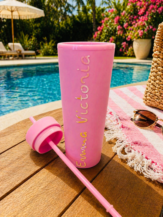 Pink custom tumbler with name with straw on a wooden table by a poolside