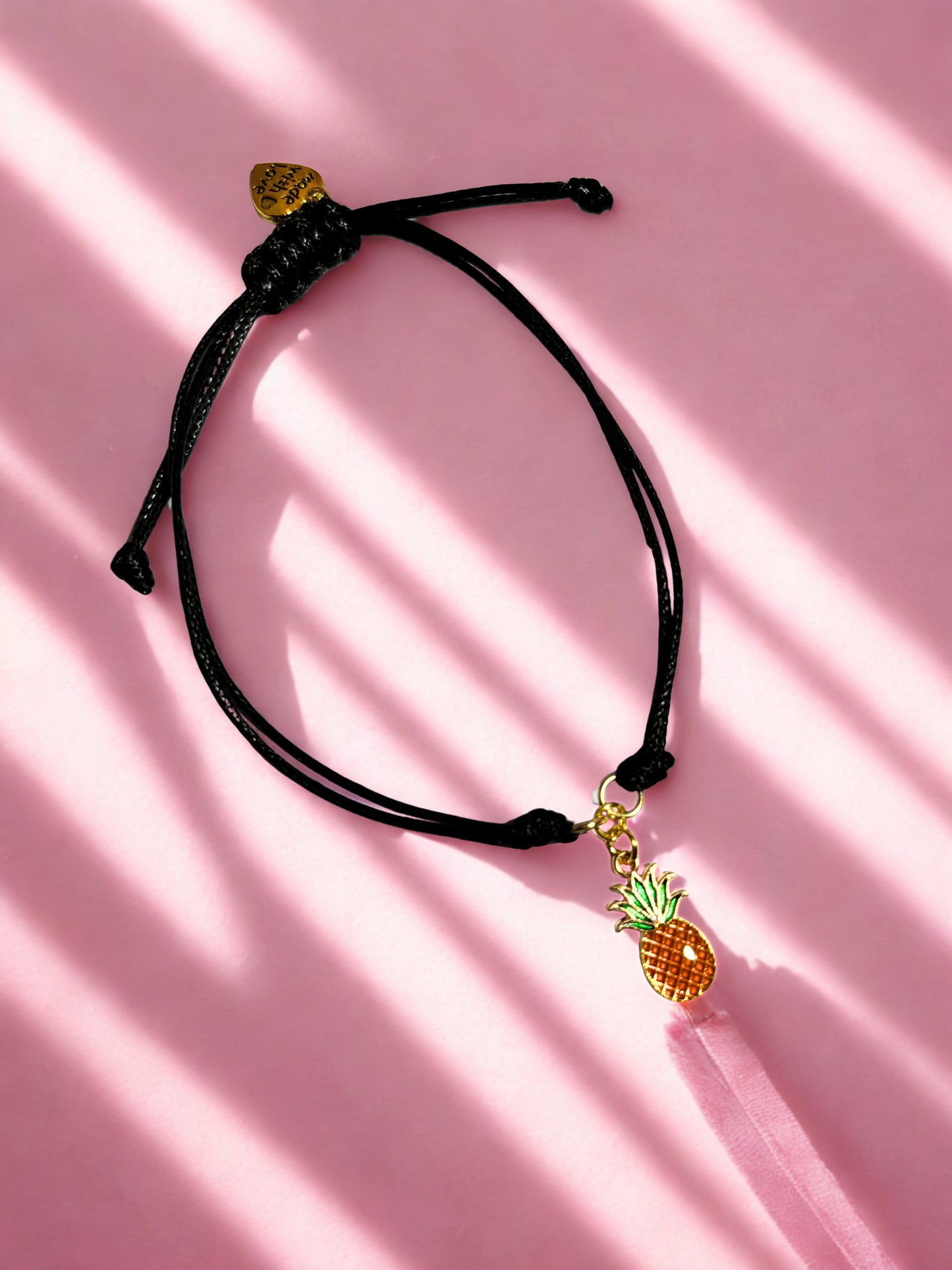 Black cord bracelet with a pineapple charm on a pink background