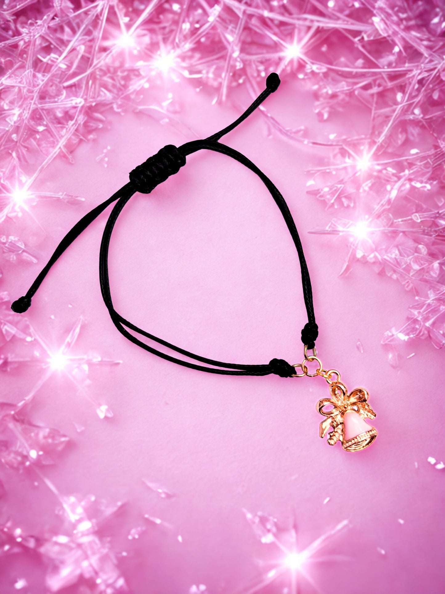 Black cord bracelet with a pink and gold bell charm on a pink glittery background