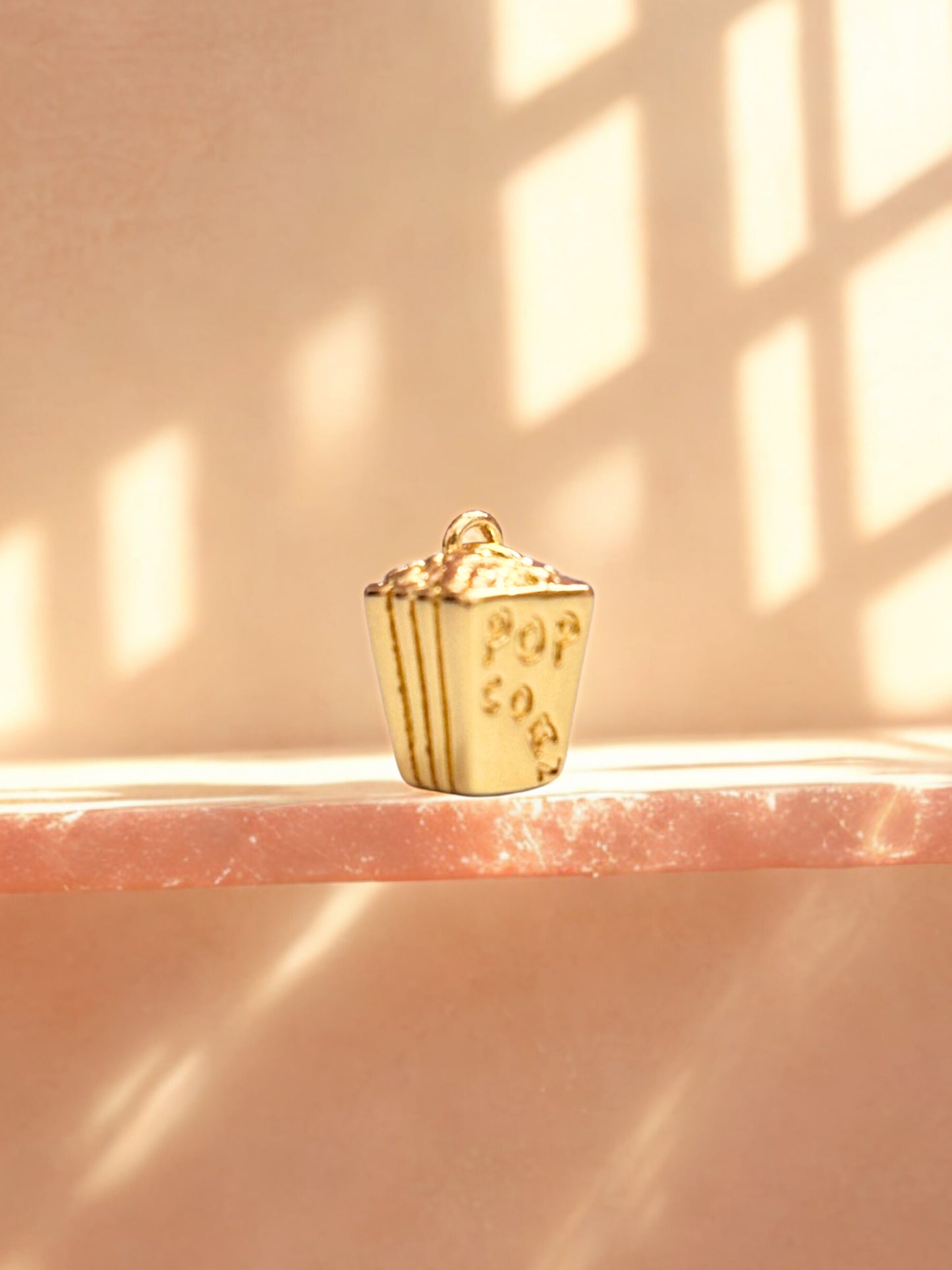 Gold popcorn bucket charm on a pink surface with soft lighting