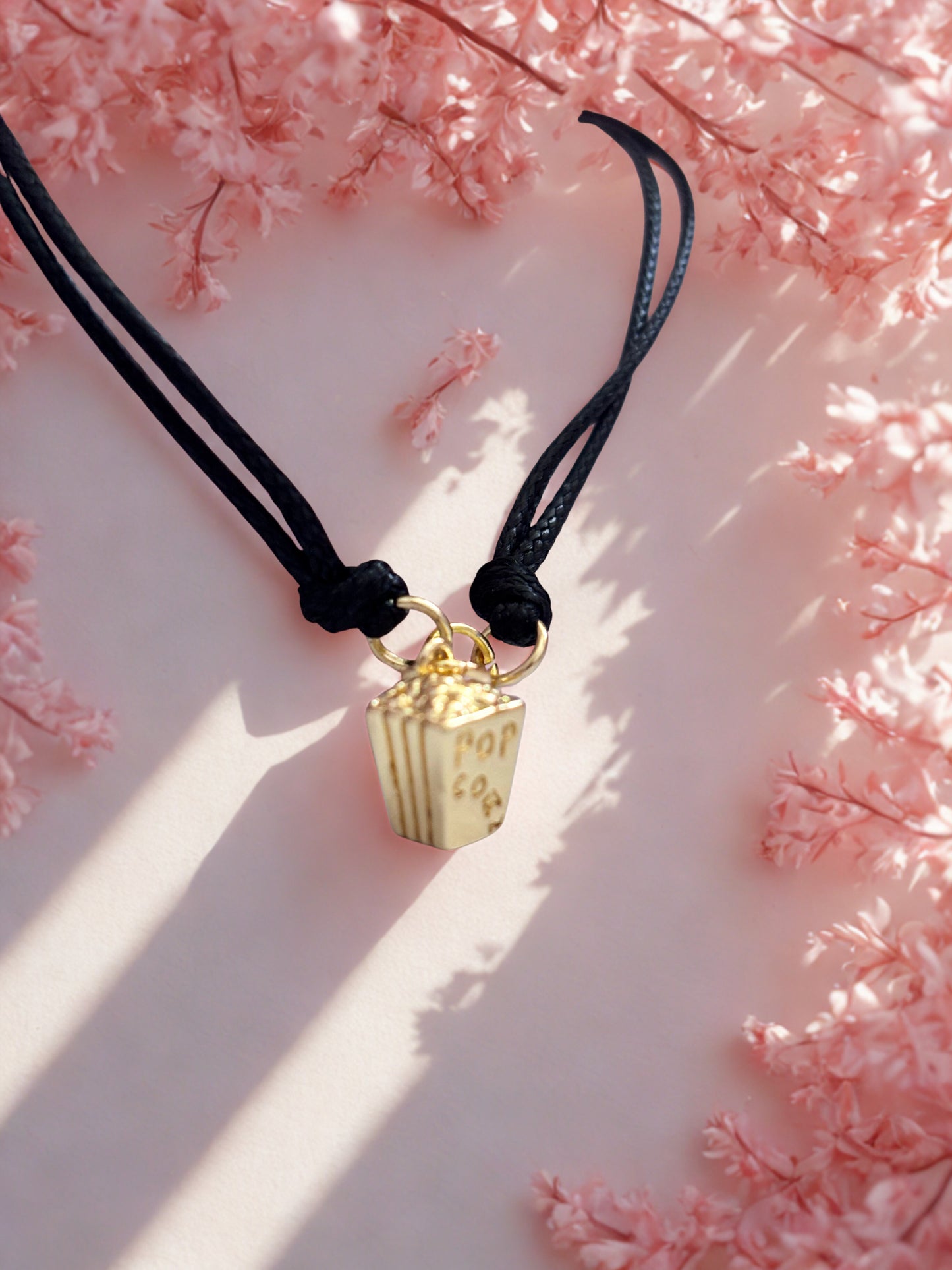 Gold popcorn charm on a black cord against a pink floral background