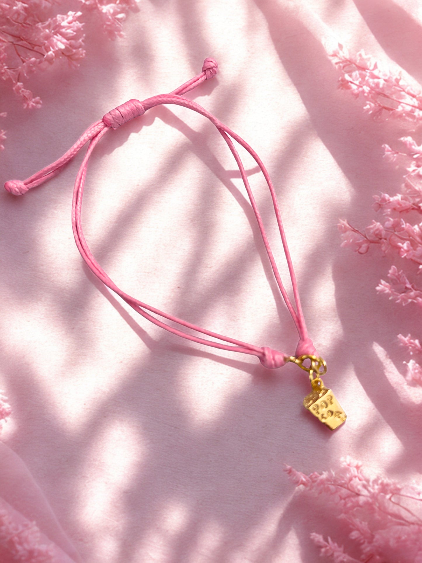 Pink bracelet with a gold popcorn charm on a pink floral background