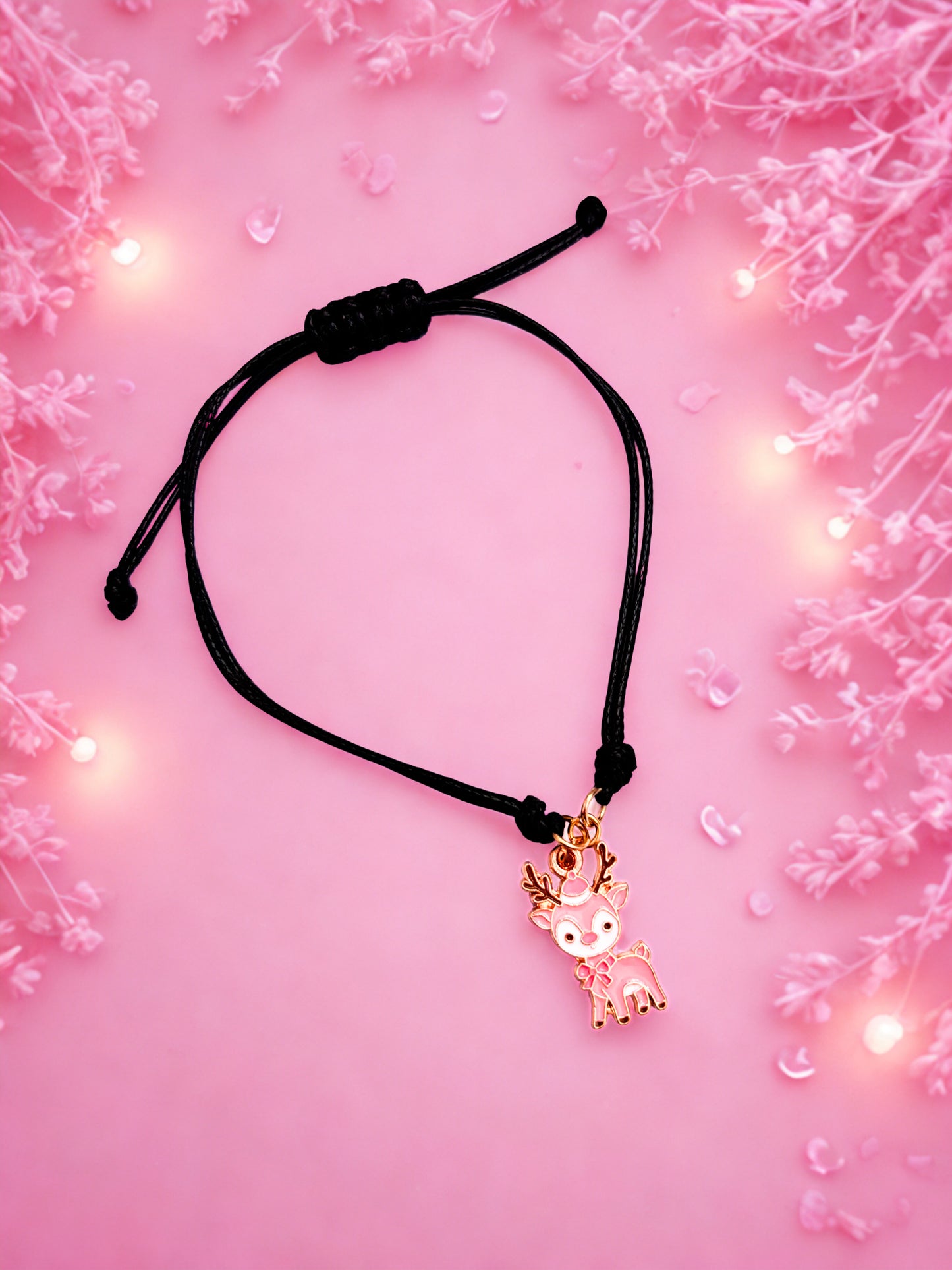 Black cord bracelet with a gold reindeer charm on a pink floral background