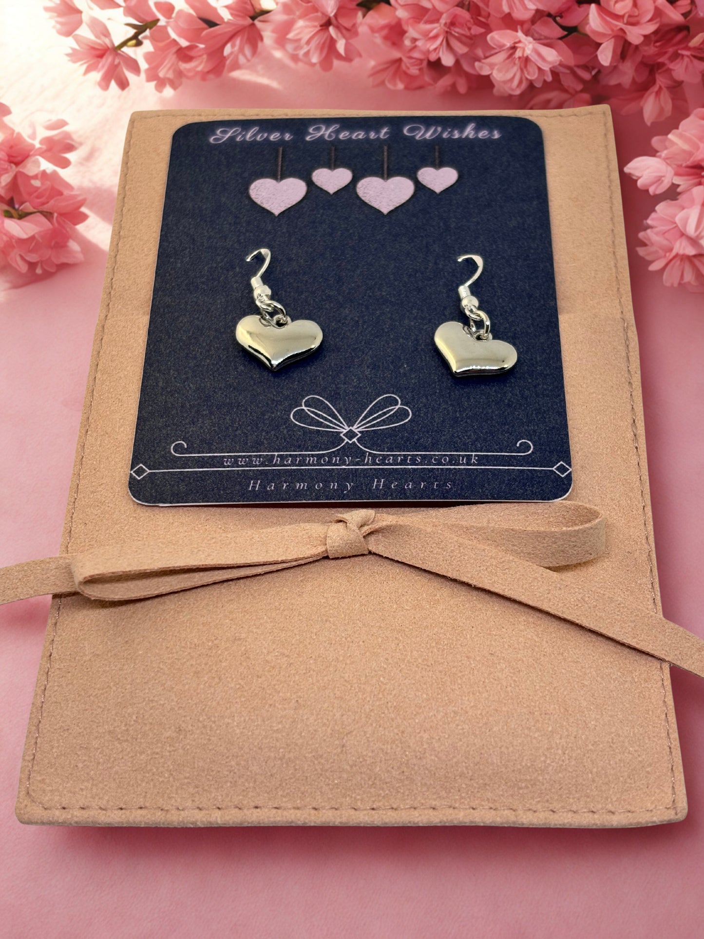 Heart-shaped earrings on a 'Silver Heart Wishes' card with pink flowers in the background