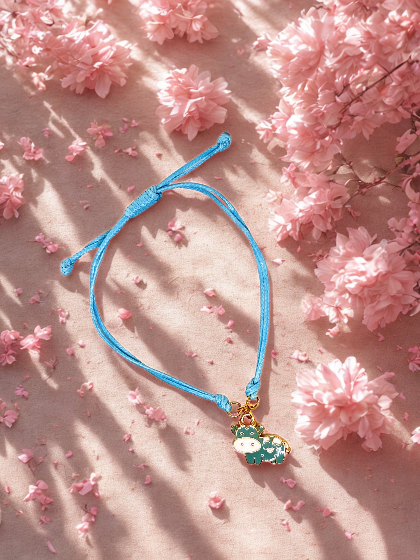Blue bracelet with a cow charm on a pink floral background