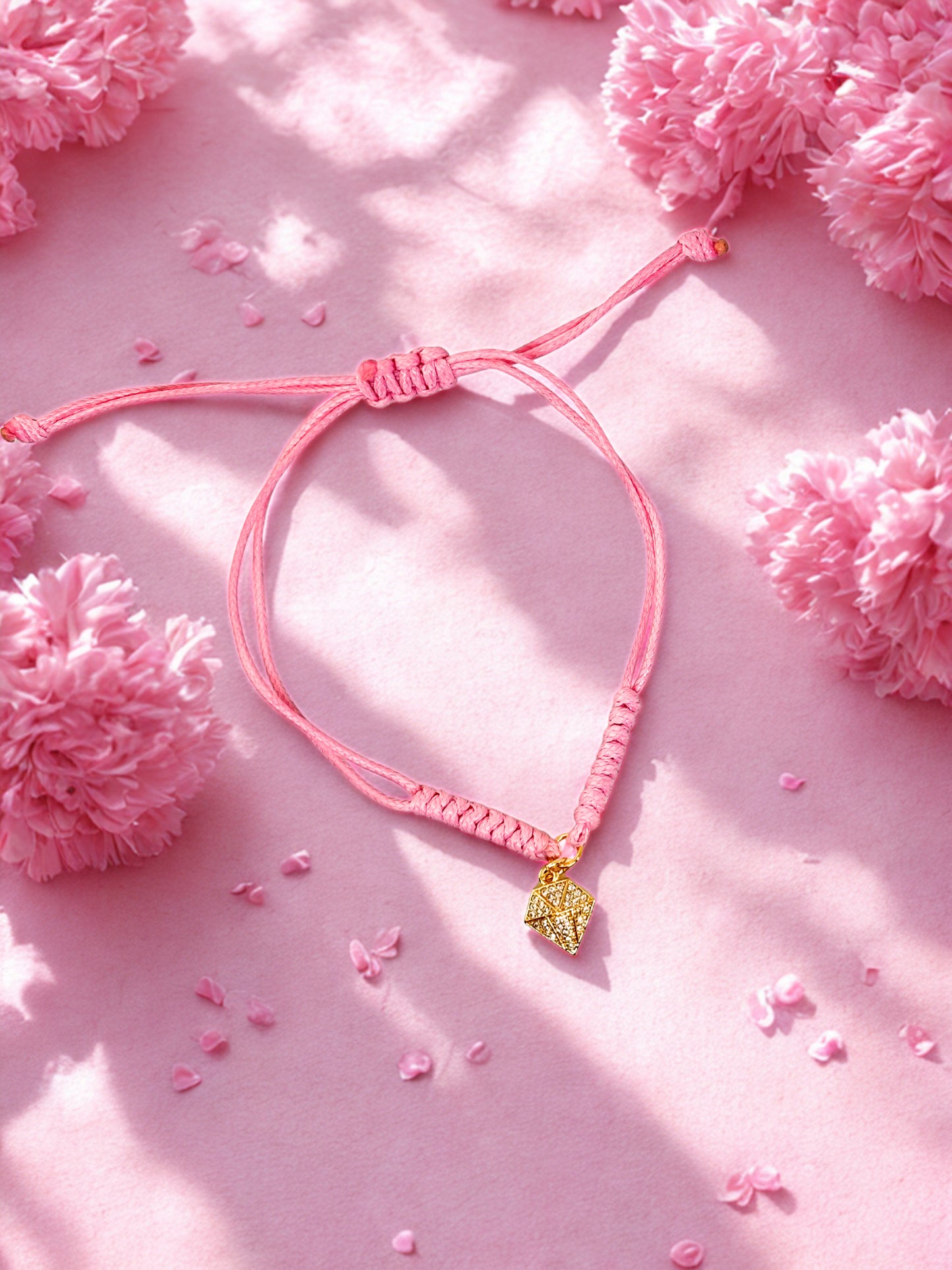 Pink bracelet with a gold diamond shape charm on a pink floral background