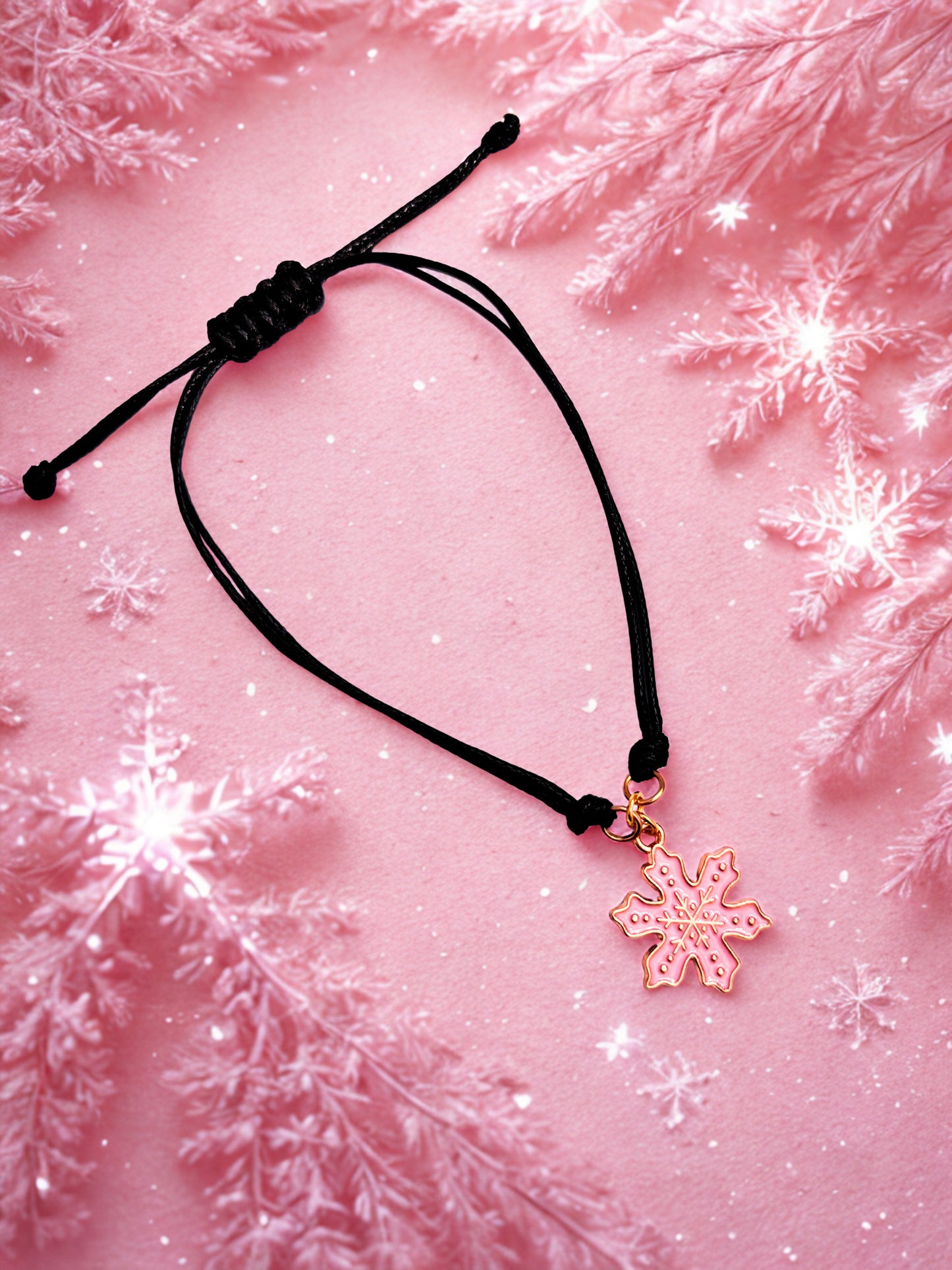 Black cord bracelet with a pink snowflake charm on a pink background with snowflake decorations