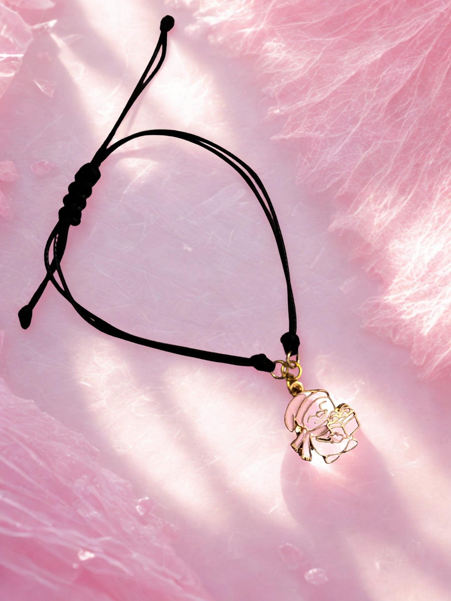 Black cord bracelet with a gold snowman charm on a pink textured background