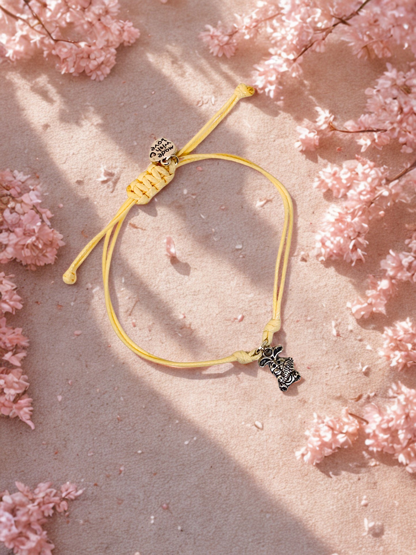 Beige bracelet cord with bunny charm on a pink floral background