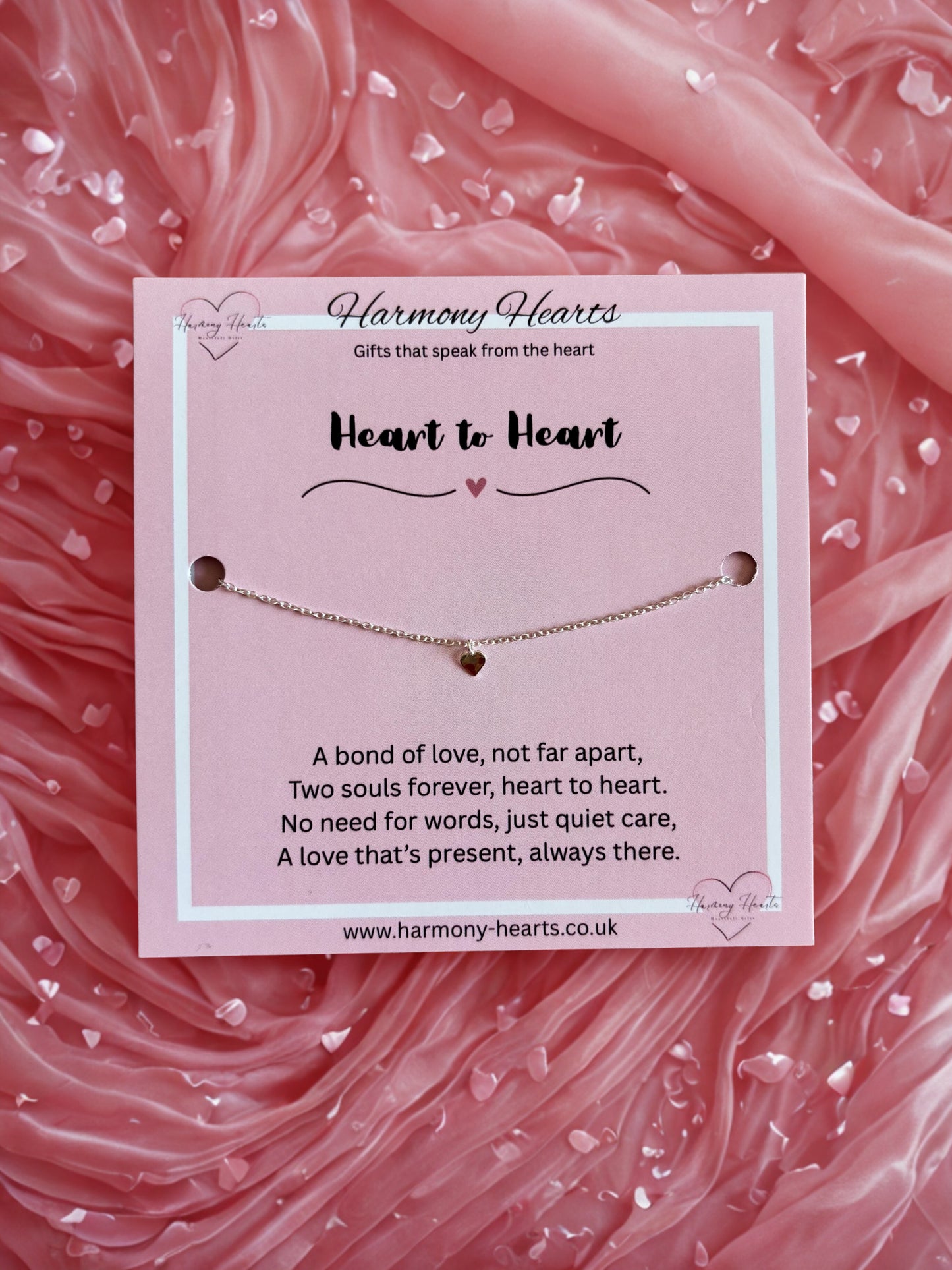Bracelet with heart charm on a pink fabric background, featuring 'Harmony Hearts' branding.