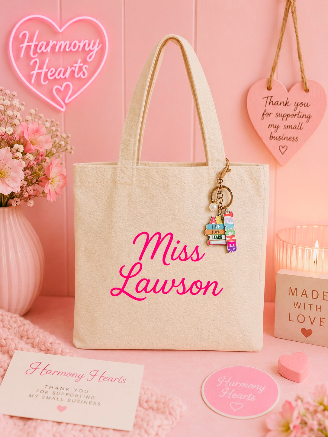 Beige tote bag with 'Miss Lawson' text, keychain, and pink heart-themed decor on a pink background.