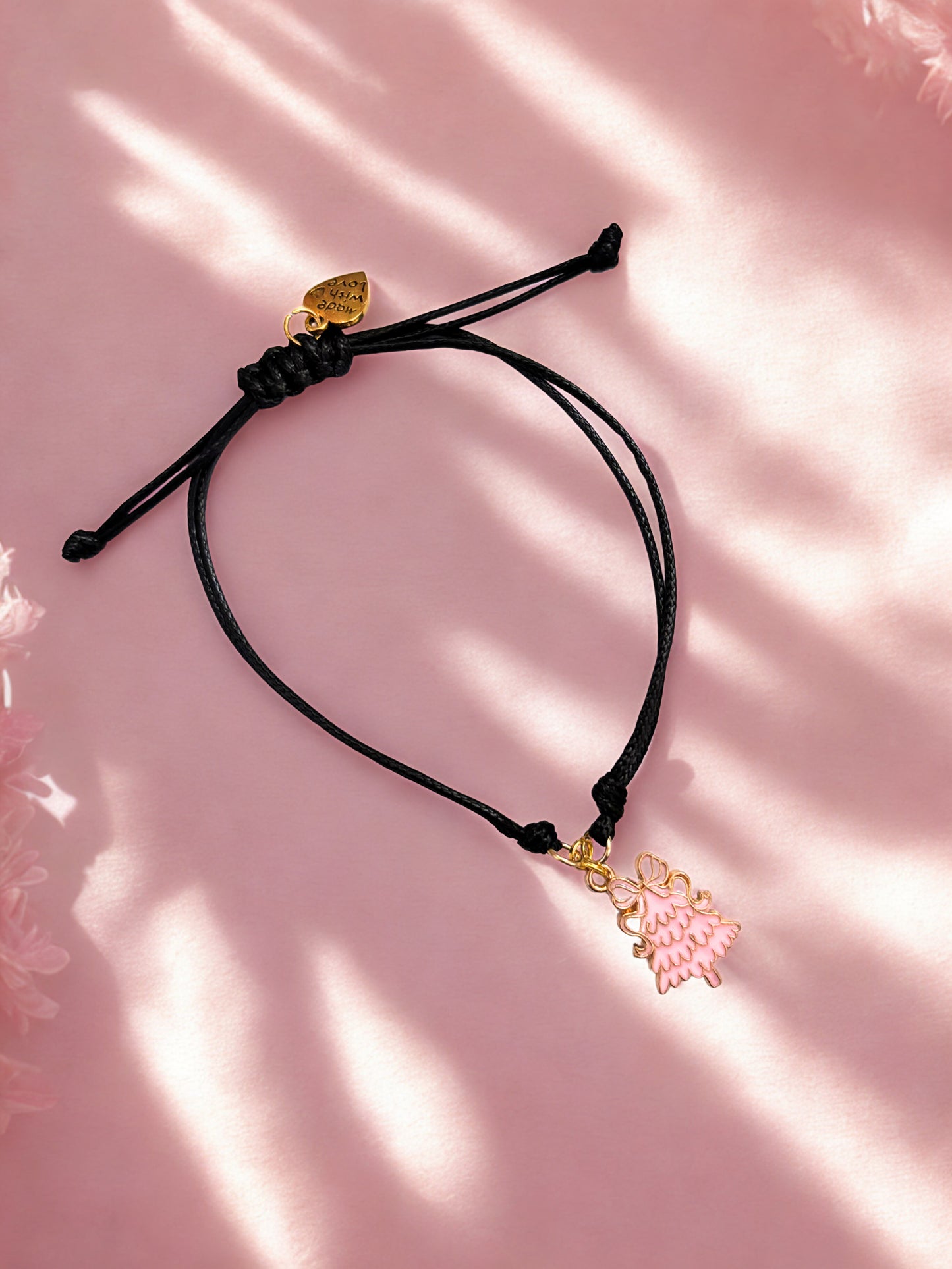Black cord charm bracelet with pink Christmas tree charm on a pink background