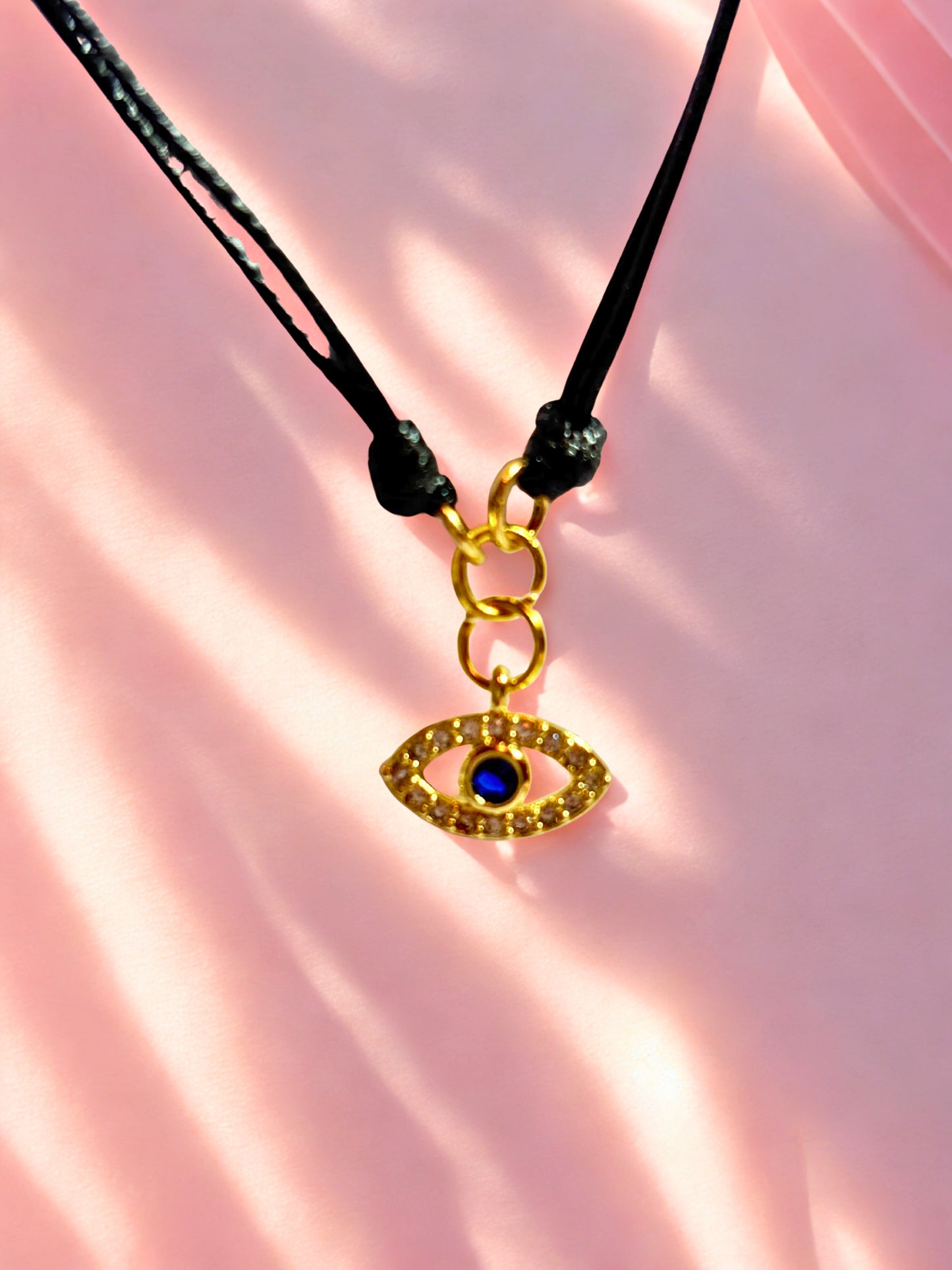 Gold evil eye charm bracelet on a pink fabric background