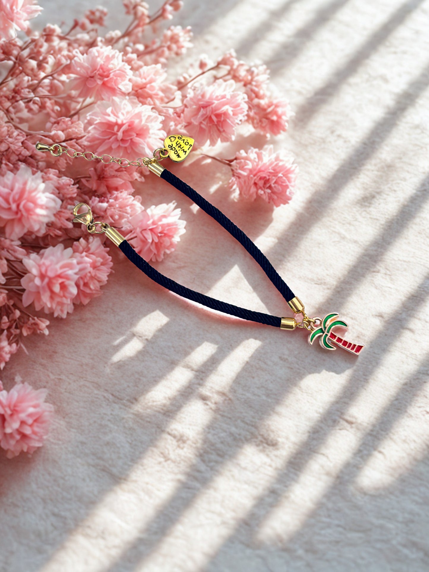 Bracelet with palm tree charm on pink flowers background