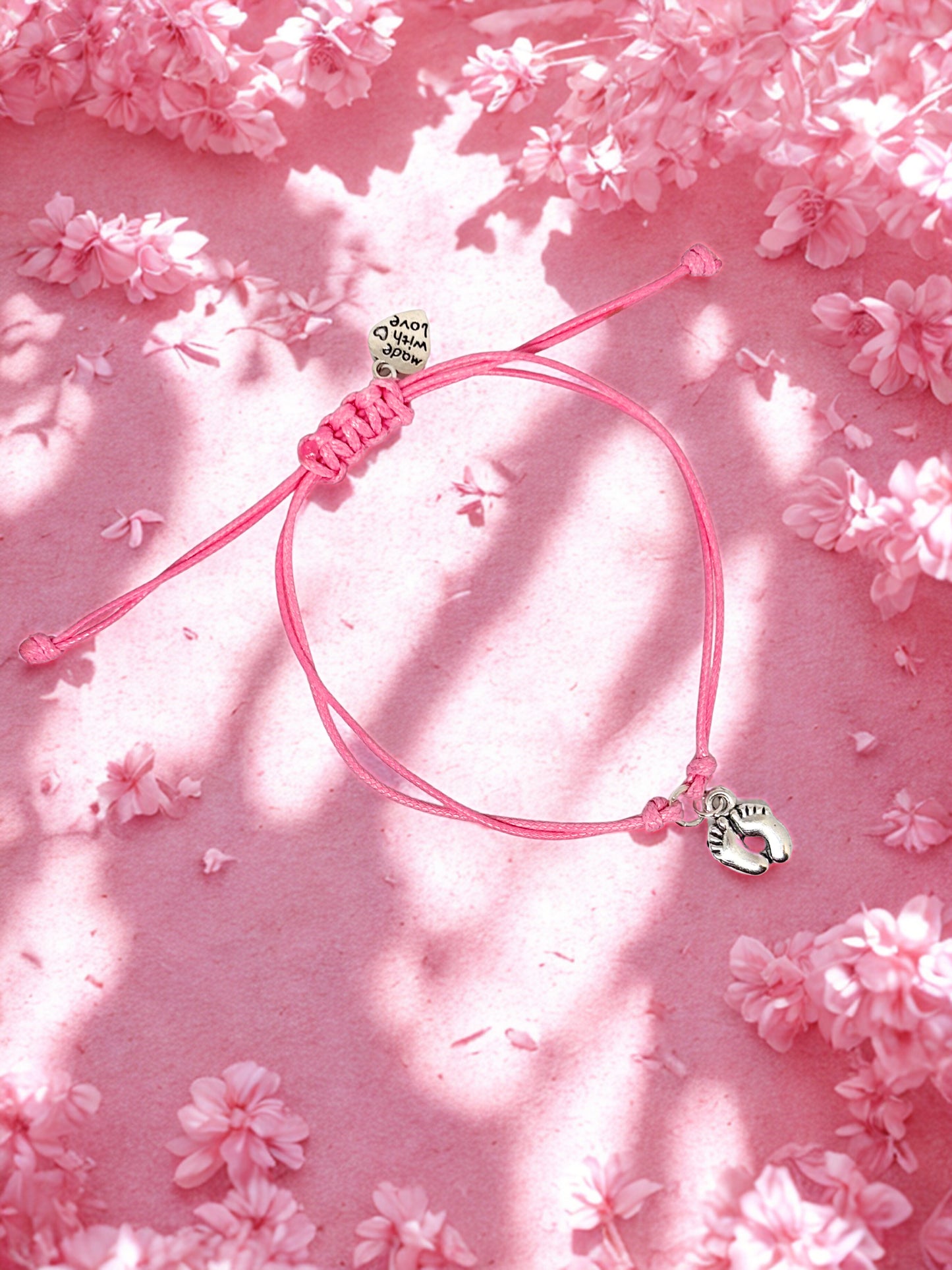 Pink bracelet with silver baby feet charm on a pink floral background