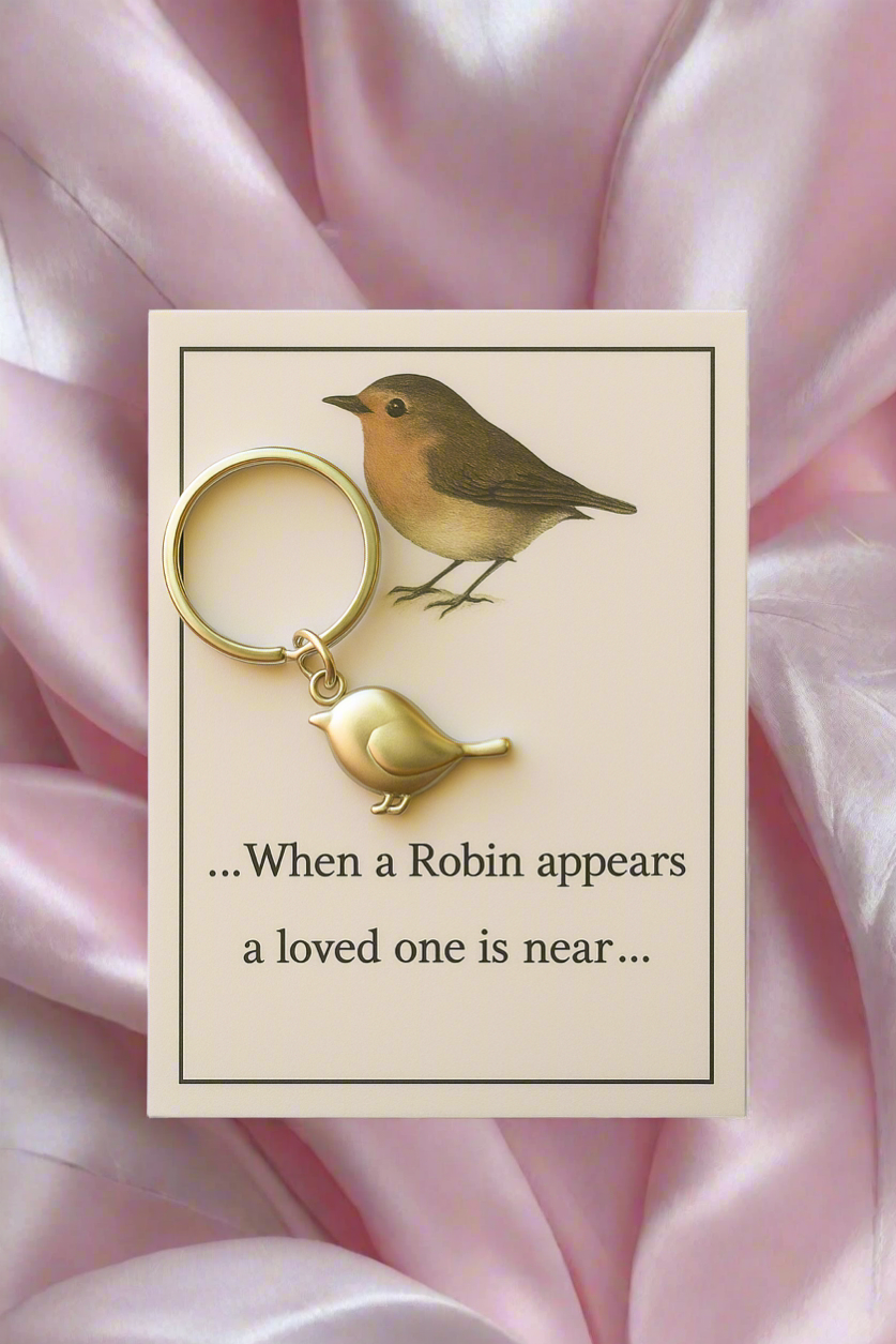 Keychain with robin design on a card with text, against a pink satin background