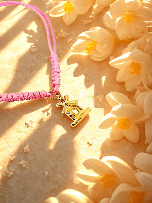 Pink cord bracelet with a gold windmill charm on a background of white flowers.