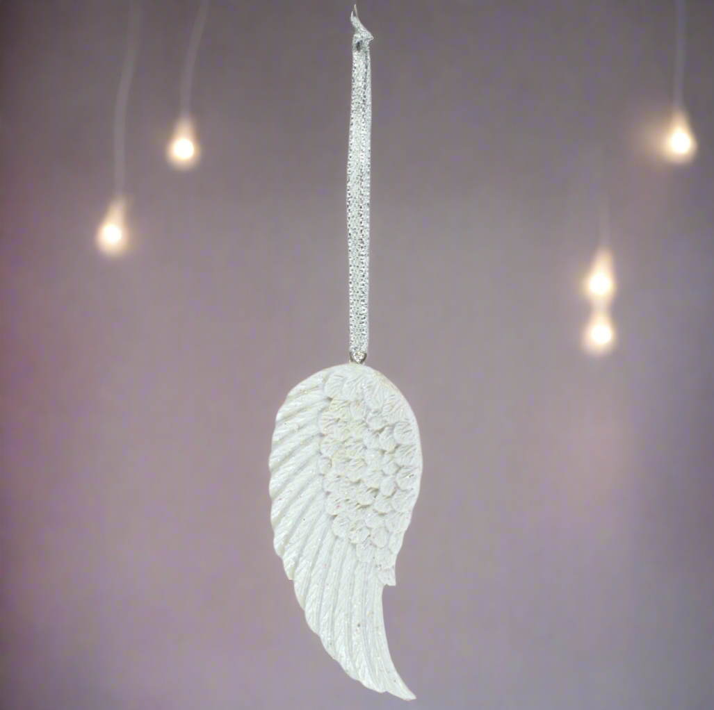 White angel wing ornament hanging against a soft, blurred background with lights.