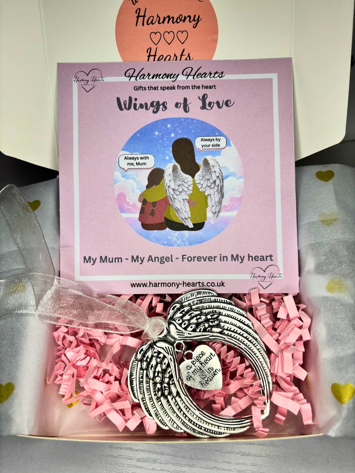 Silver angel wing ornament in a box with pink tissue paper and a 'Harmony Hearts' card.