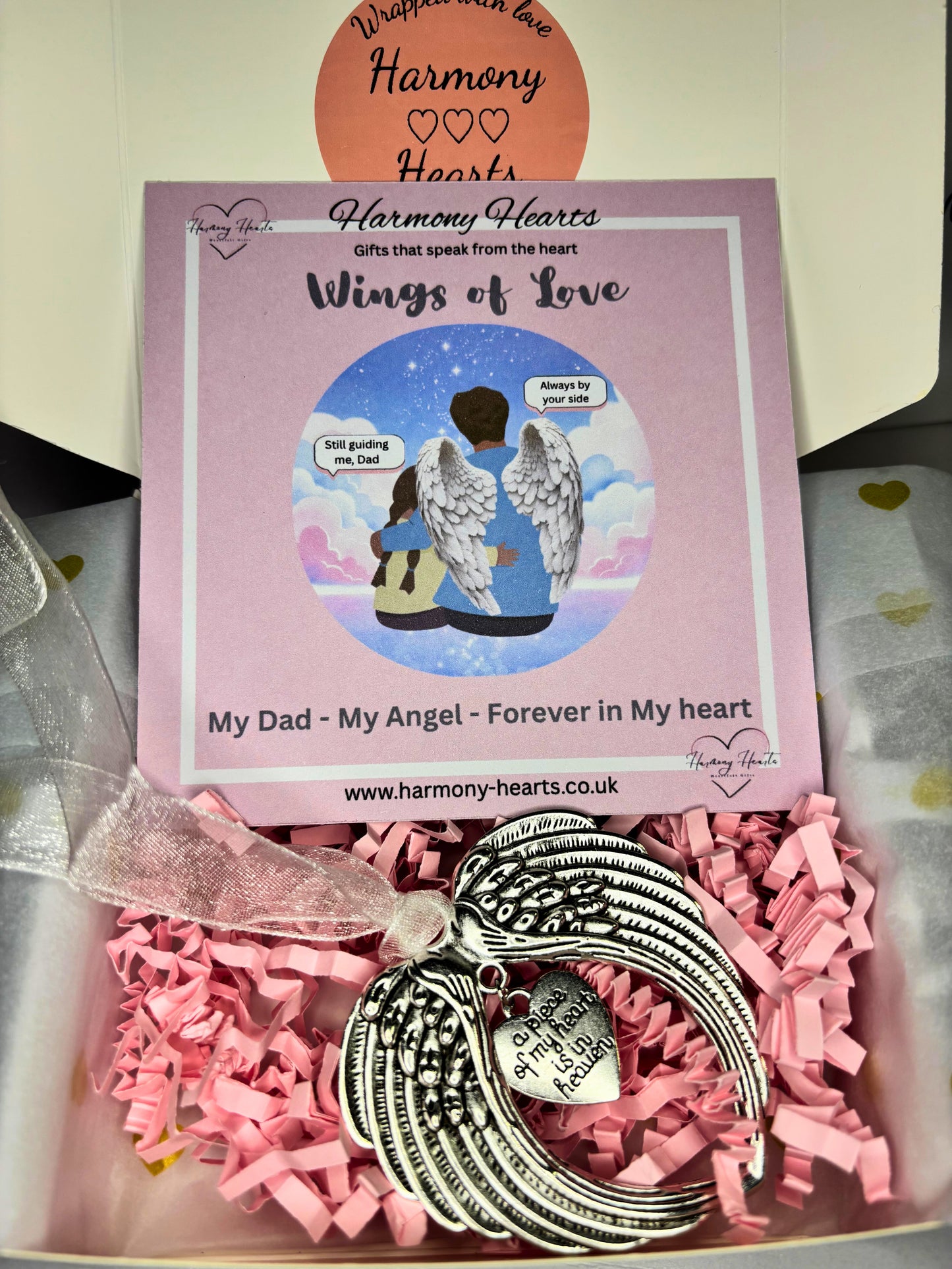 Wings of Love ornament in a box with pink tissue paper and Harmony Hearts packaging.